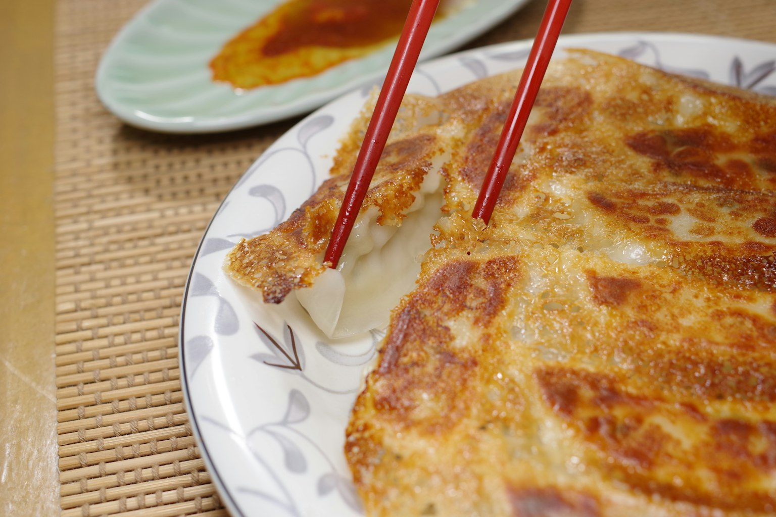 A plate of crispy gyoza with red chopsticks lifting a piece and a dish of sauce