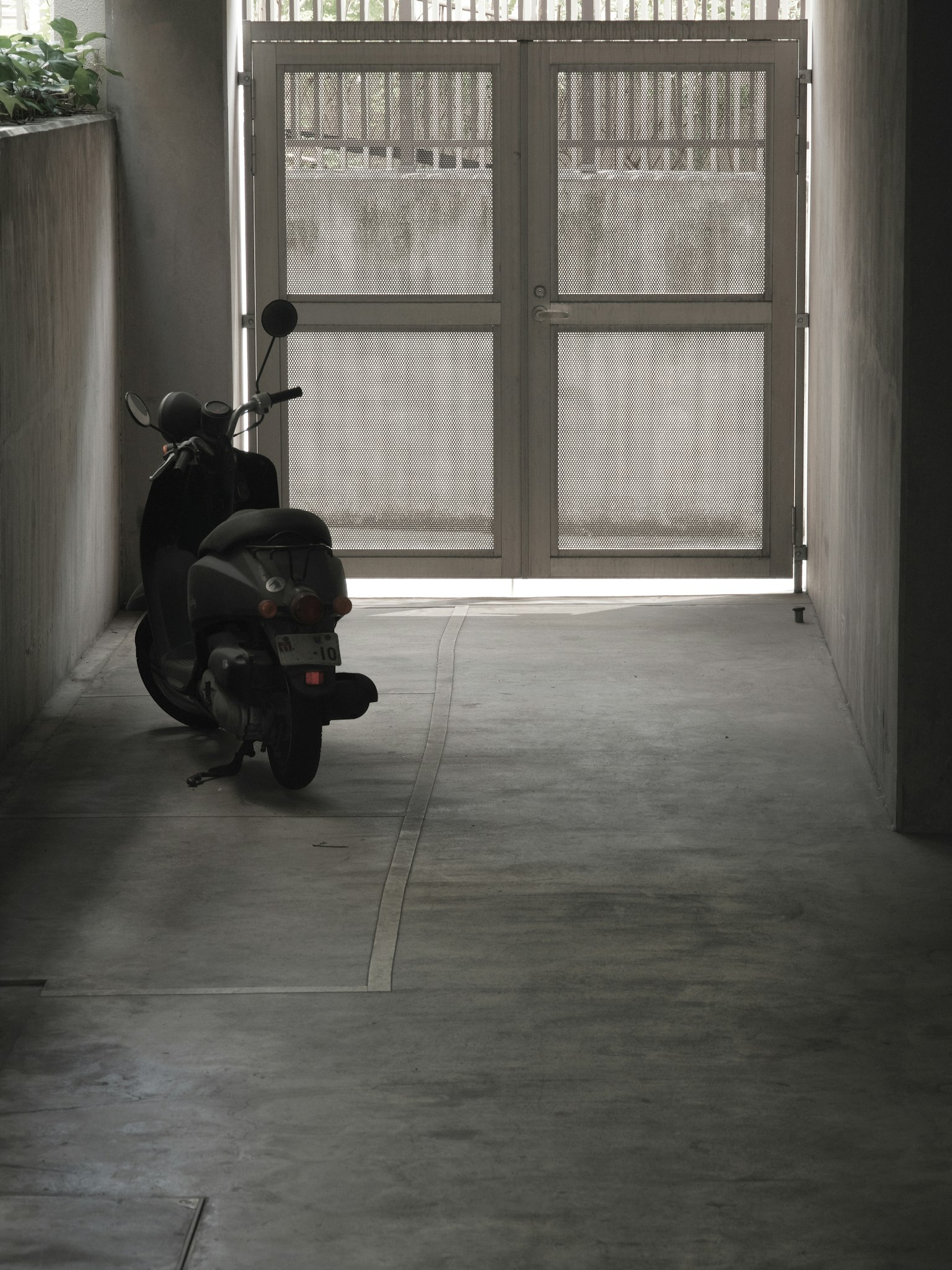 Skuter diparkir di koridor gelap dengan cahaya masuk dari pintu