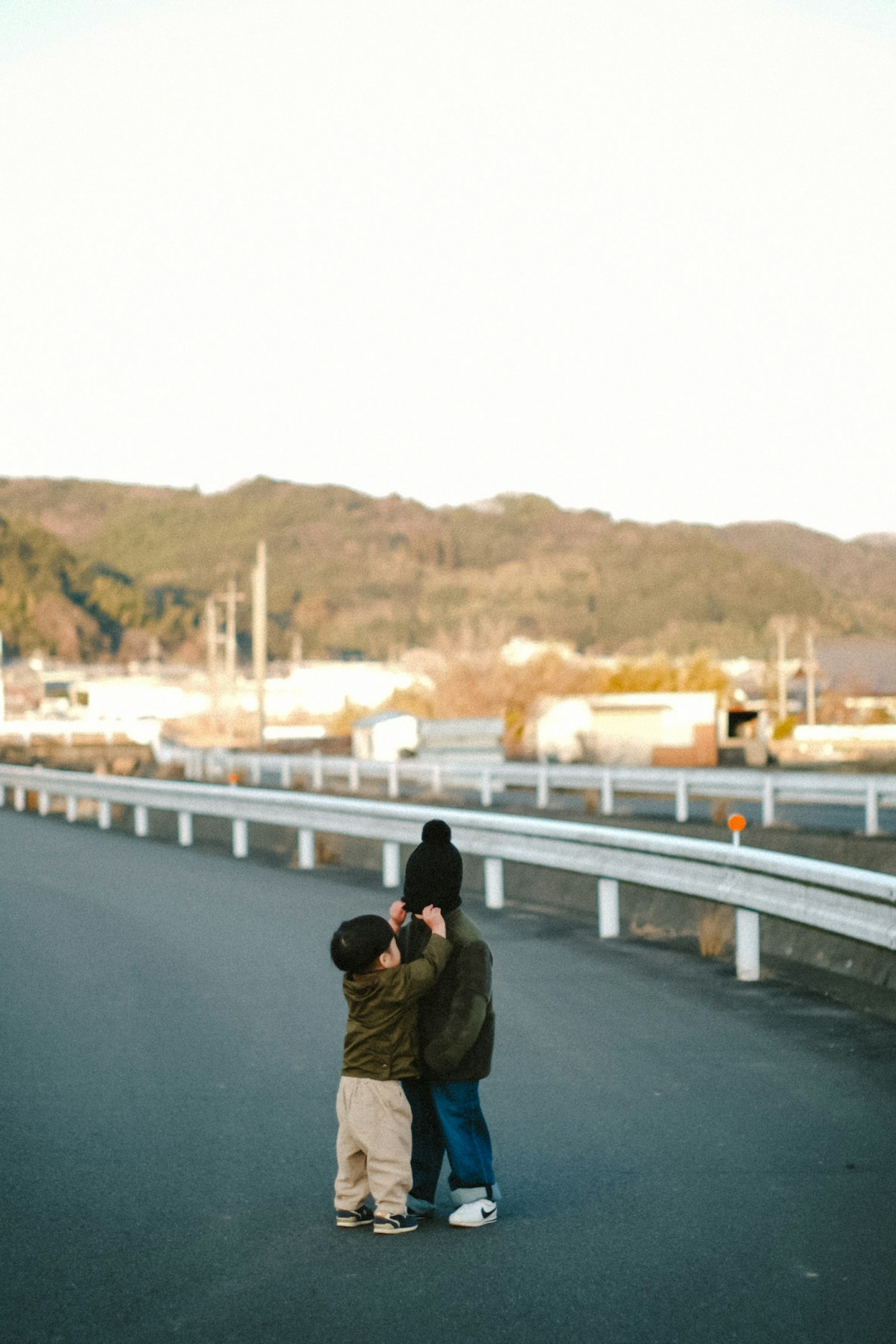 Two children playing in the middle of a road with mountains and factories in the background