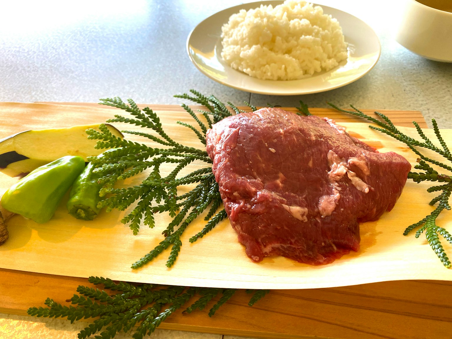 Fresh meat and vegetables arranged on a plate with rice in the background