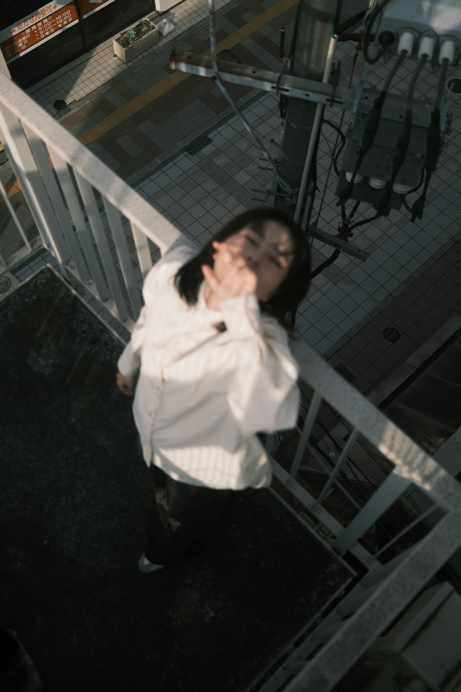 屋上のバルコニーでポーズを取る女性 白いシャツと黒いパンツを着用 髪が風になびいている