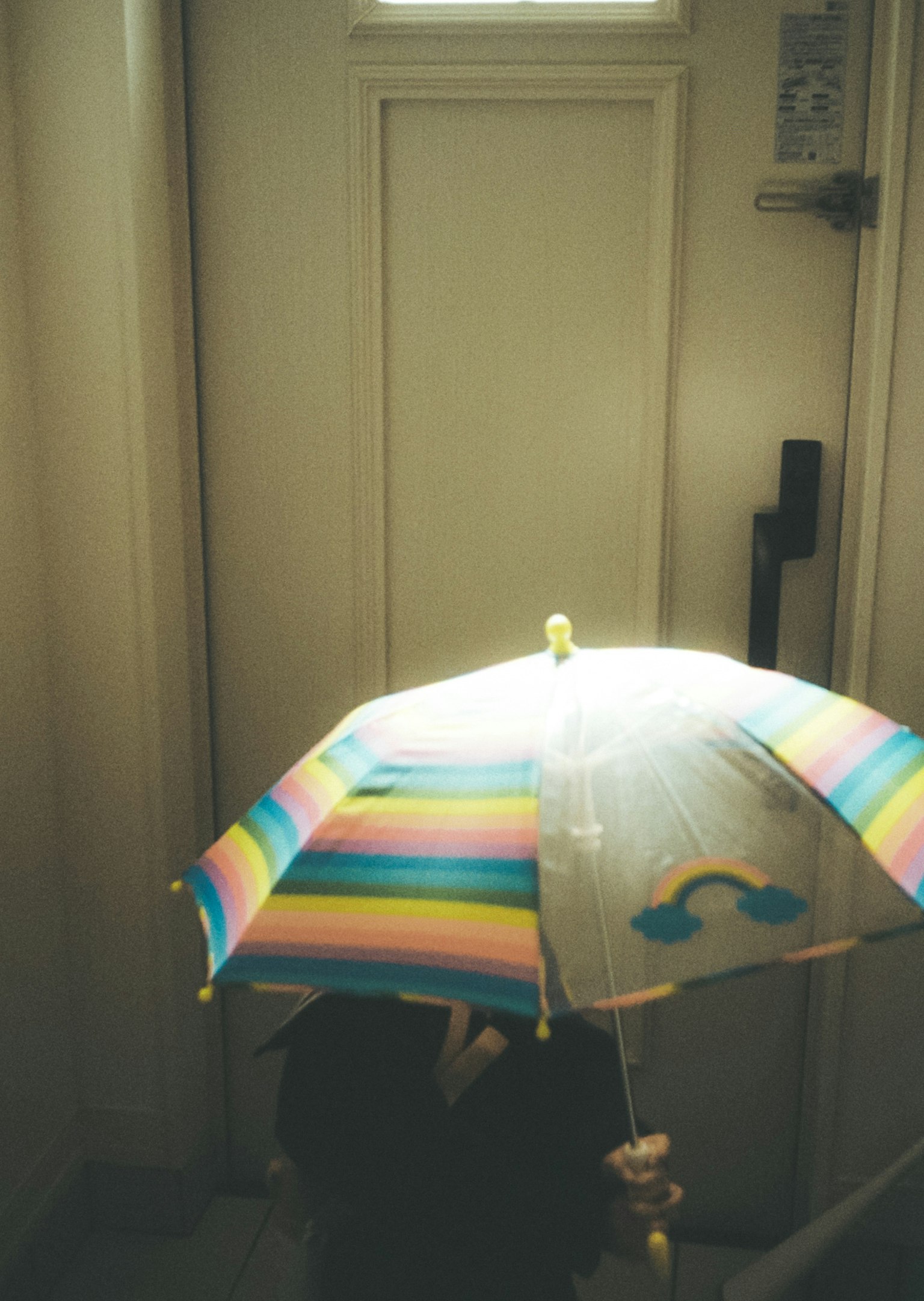 Una persona con un ombrello colorato davanti a una porta