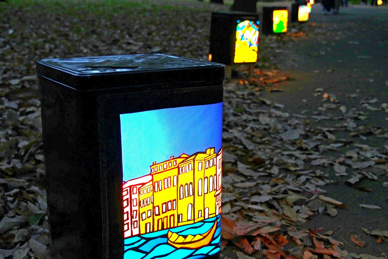 Eine Reihe bunter Laternen mit künstlerischen Designs auf einem von fallenden Blättern bedeckten Weg