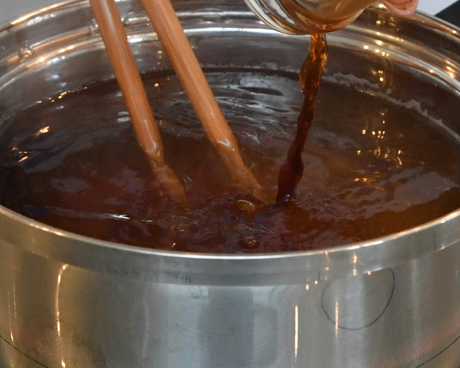 Ein dunkles Getränk in einen Topf gießen mit Holzstäbchen