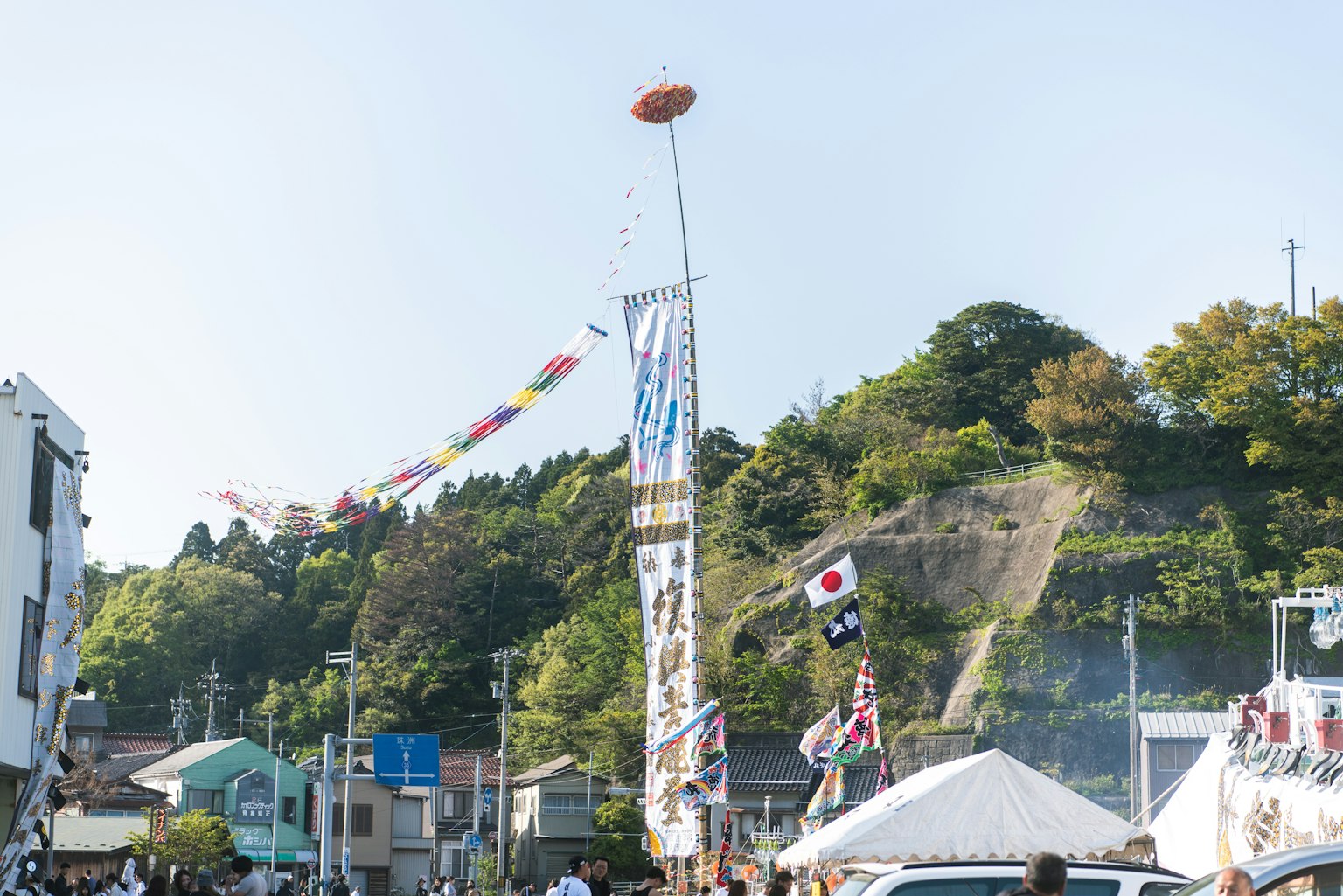 Festival scene featuring a tall pole with colorful flags and a hill in the background