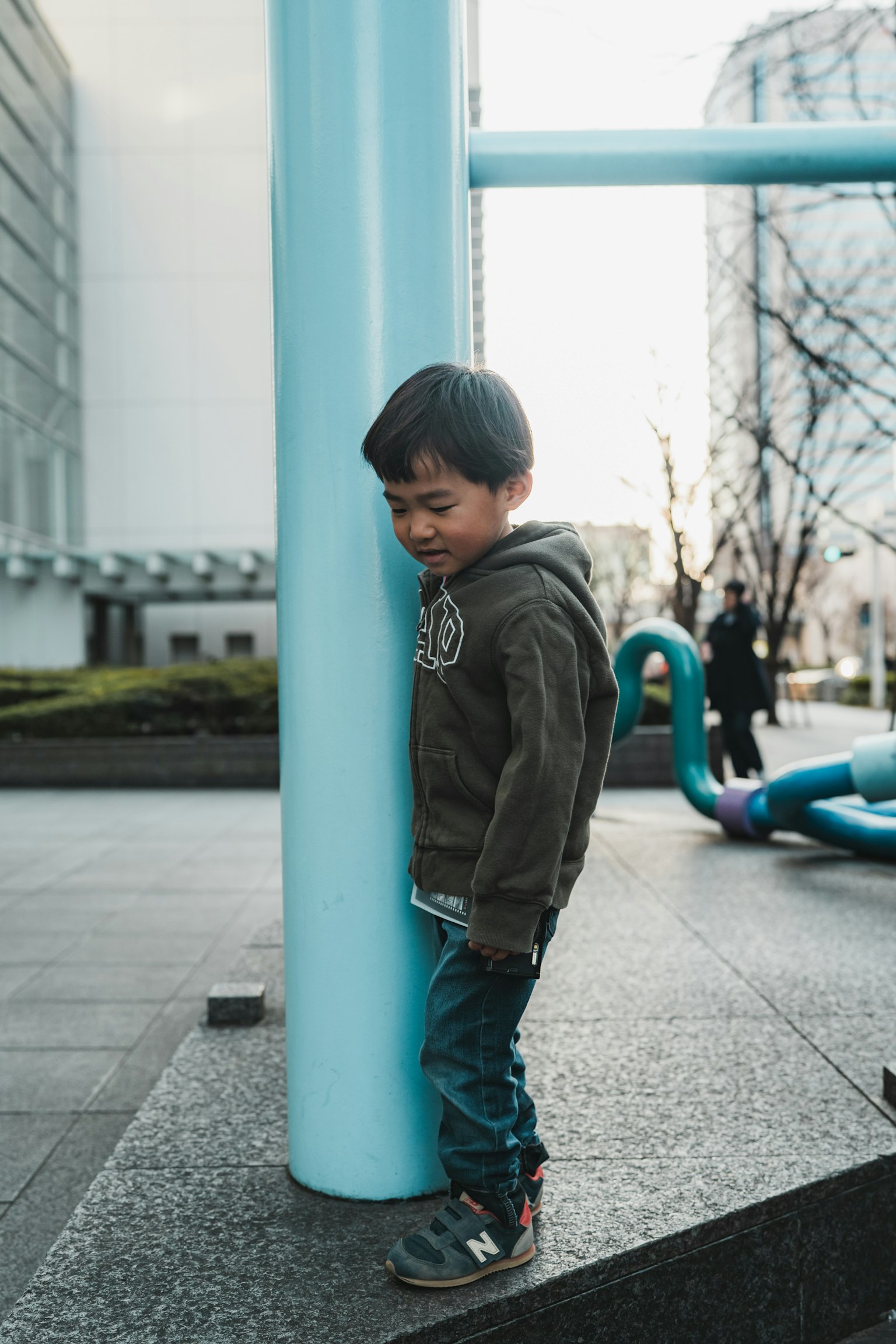 孩子靠在藍色柱子上，背景有遊樂設施