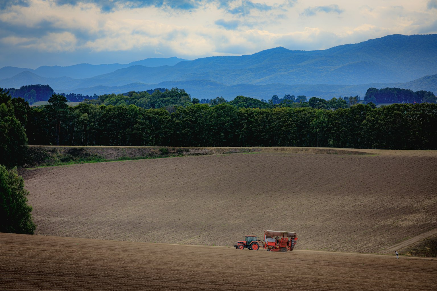 Paysage de terres agricoles vastes avec un tracteur au premier plan et des montagnes en arrière-plan