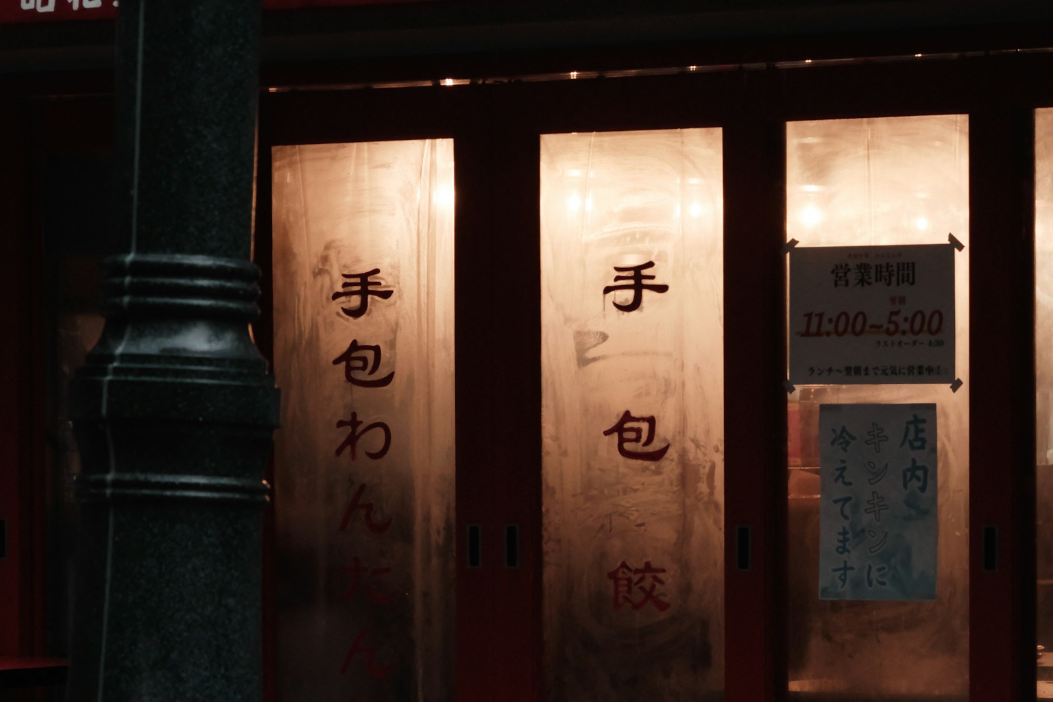 ภายนอกของร้านอาหารที่มีประตูไม้แดงที่มีตัวอักษรเขียนด้วยมือ