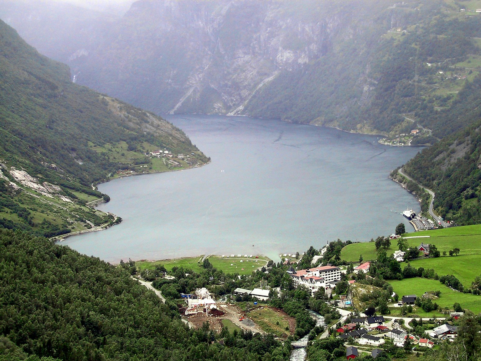 Malersicher Blick auf einen Fjord umgeben von üppigen Bergen und einem kleinen Dorf