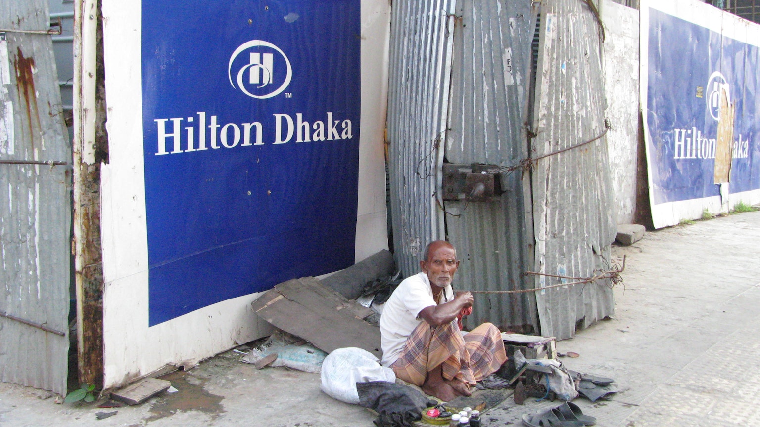 Người đàn ông vô gia cư ngồi trước biển hiệu Hilton Dhaka