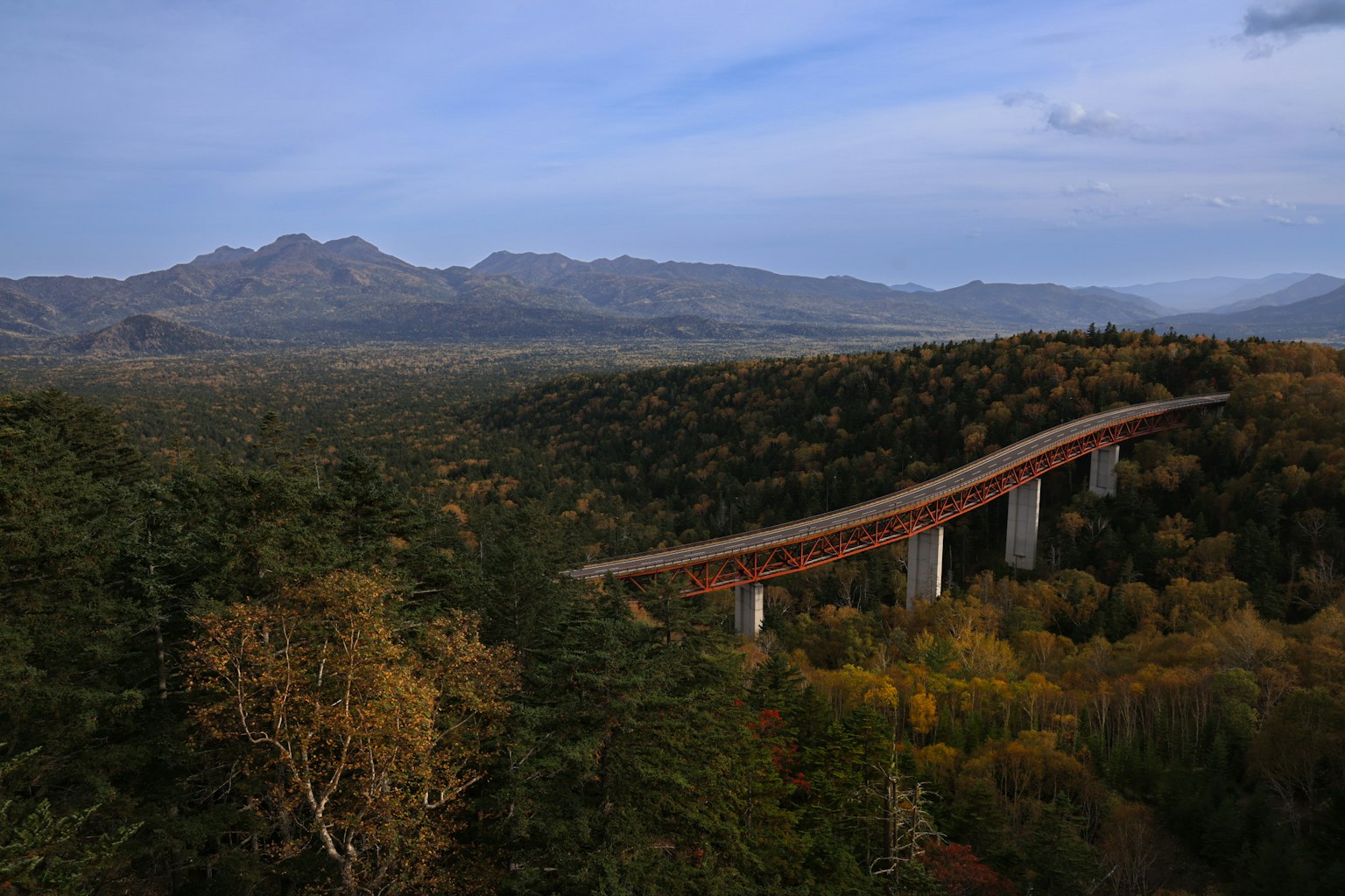 Scenic view of an elevated bridge with mountains in the background mixed with green and autumn colors
