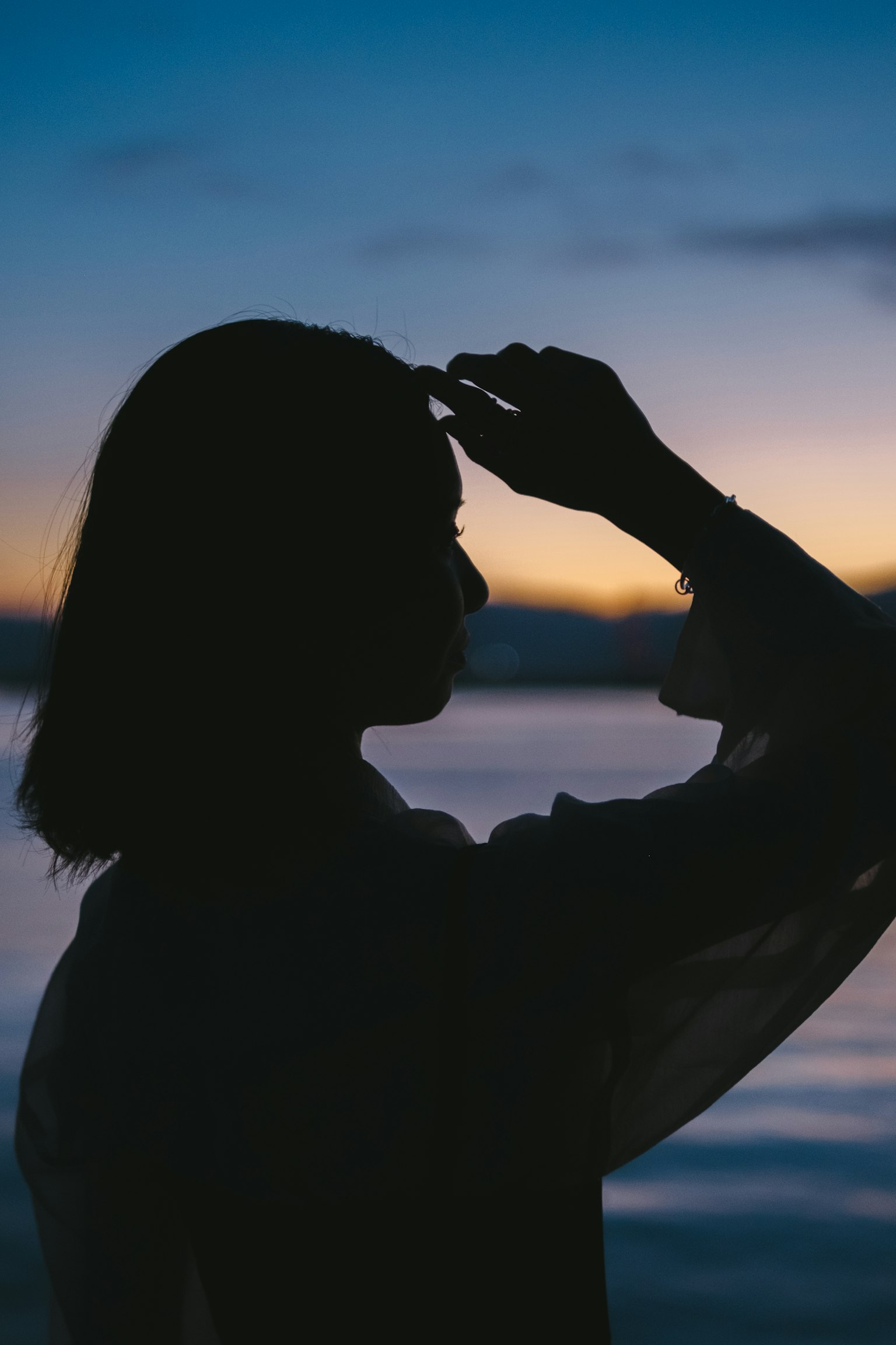 Silhouette d'une femme tenant sa main sur son front au crépuscule près de la mer
