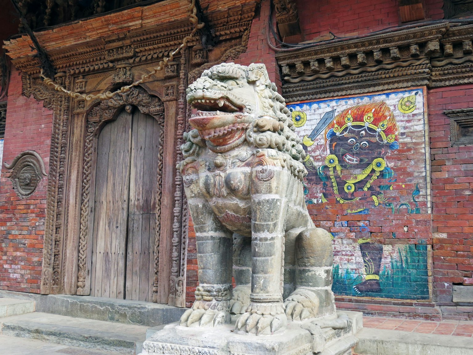 Statue de lion en pierre devant un temple avec une fresque colorée