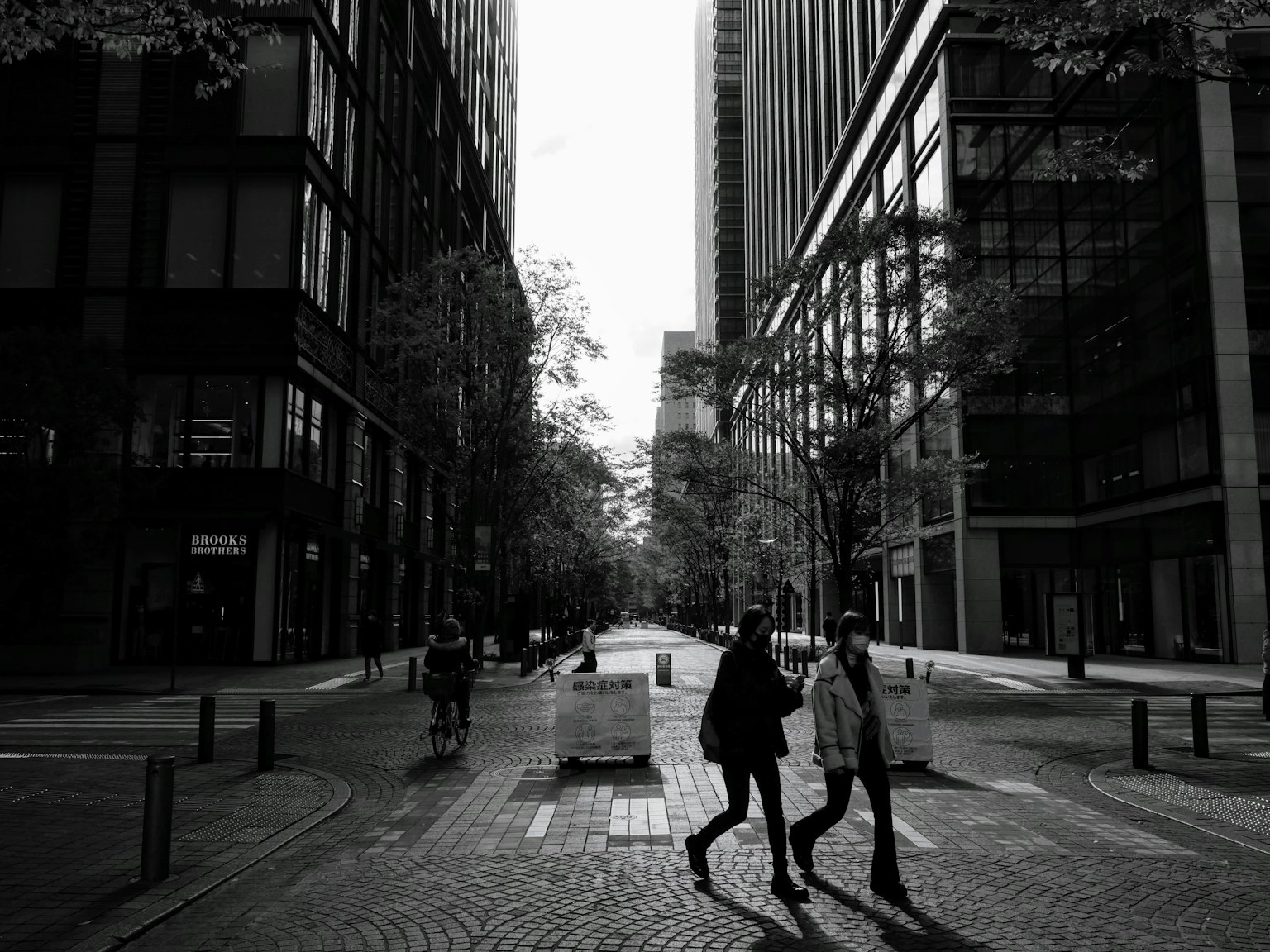 Paysage urbain en noir et blanc avec deux personnes traversant une rue entre des bâtiments