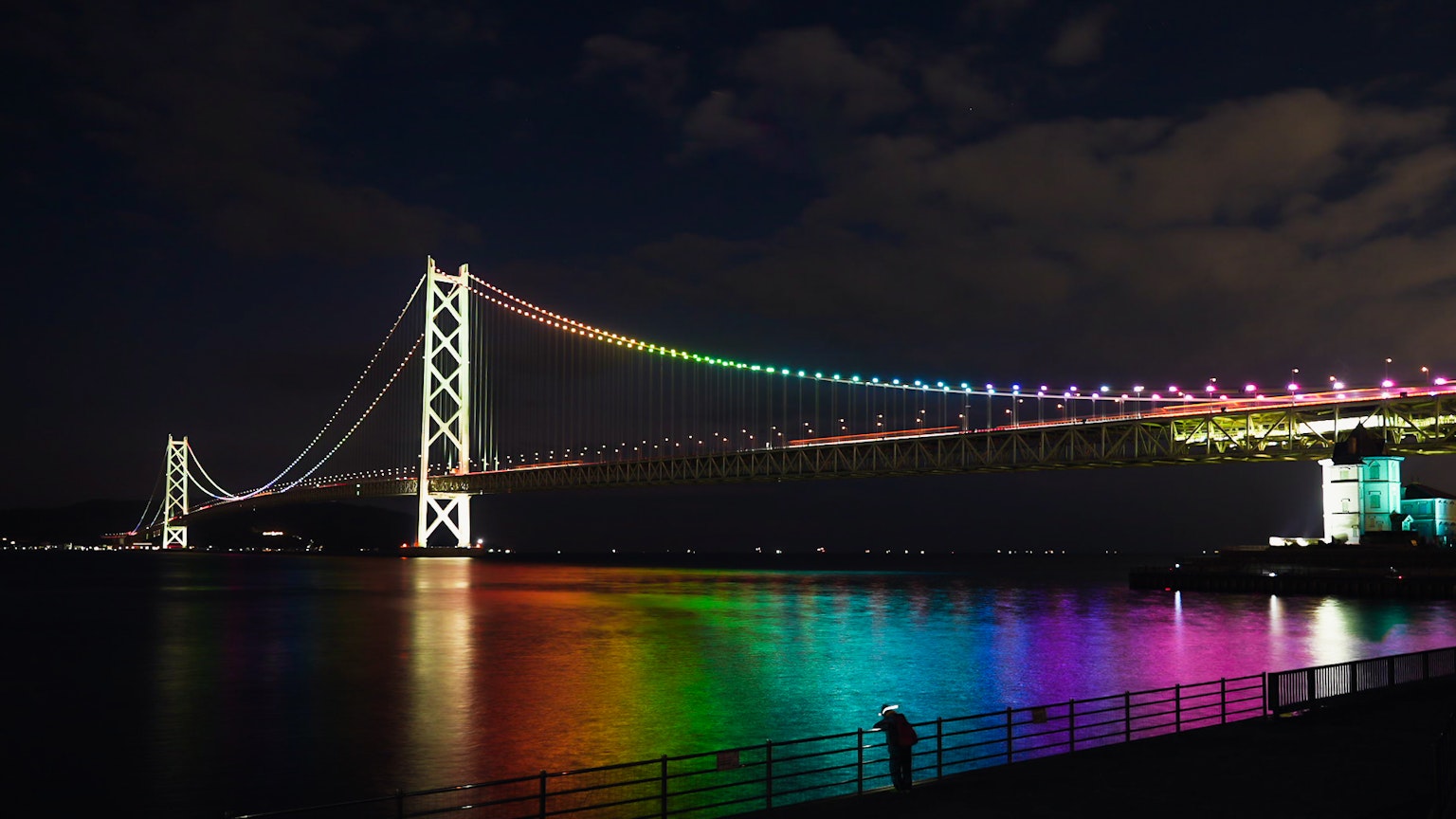 Ponte illuminato di arcobaleno di notte con riflessi sull'acqua