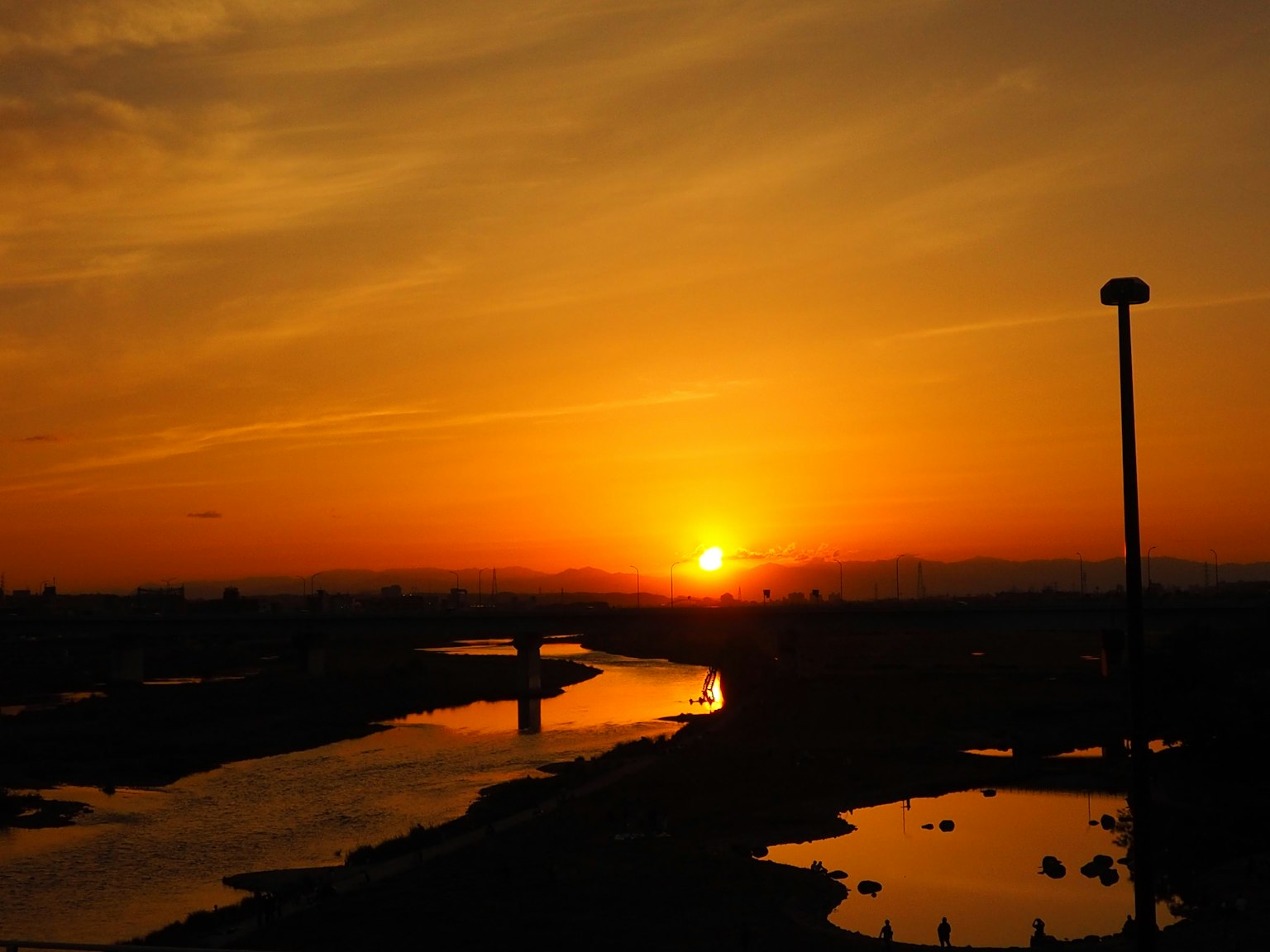 Coucher de soleil sur une rivière avec un ciel orange des reflets sur l'eau et un pont et un lampadaire visibles