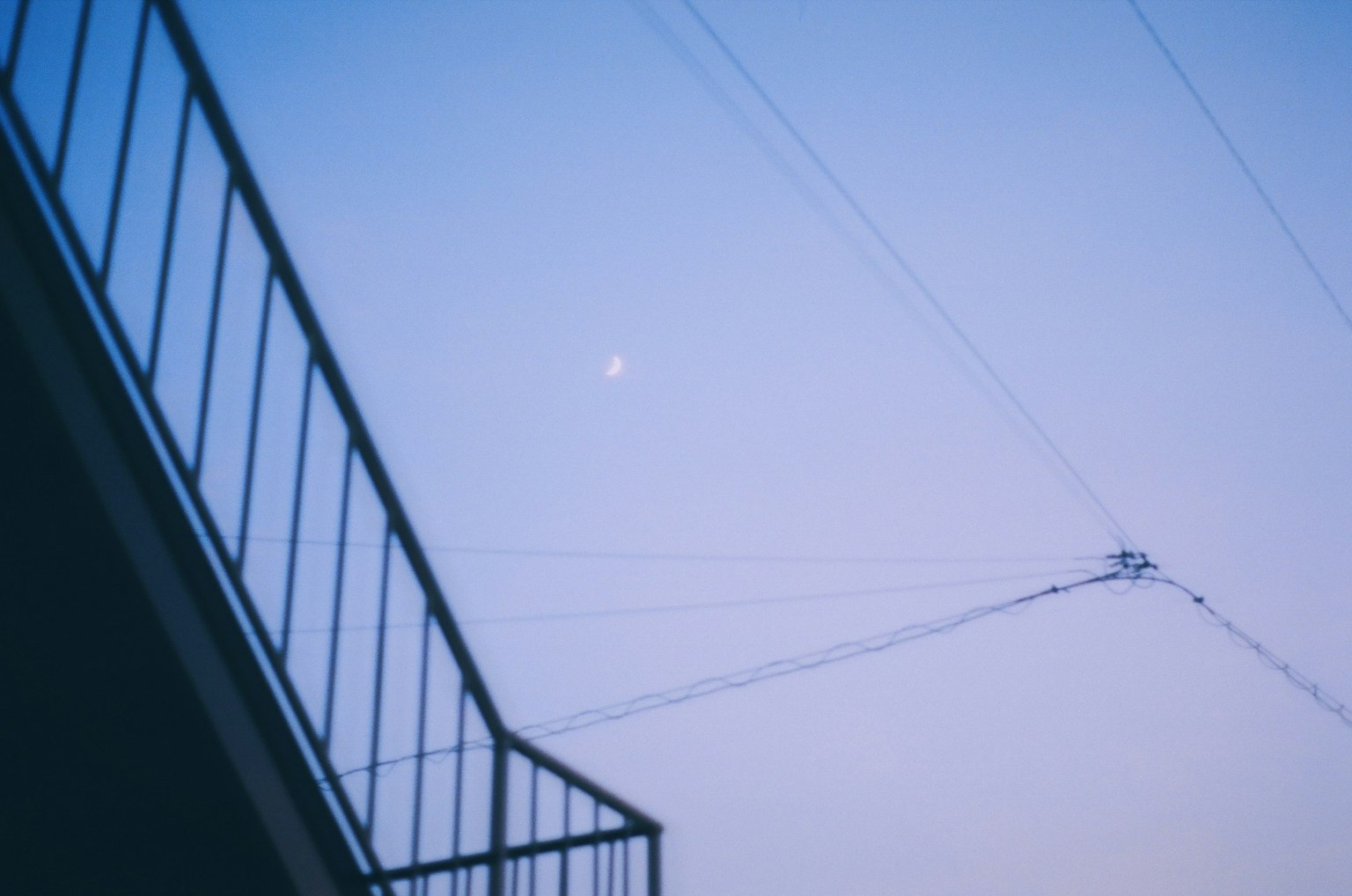 A view of the moon in a blue sky with power lines