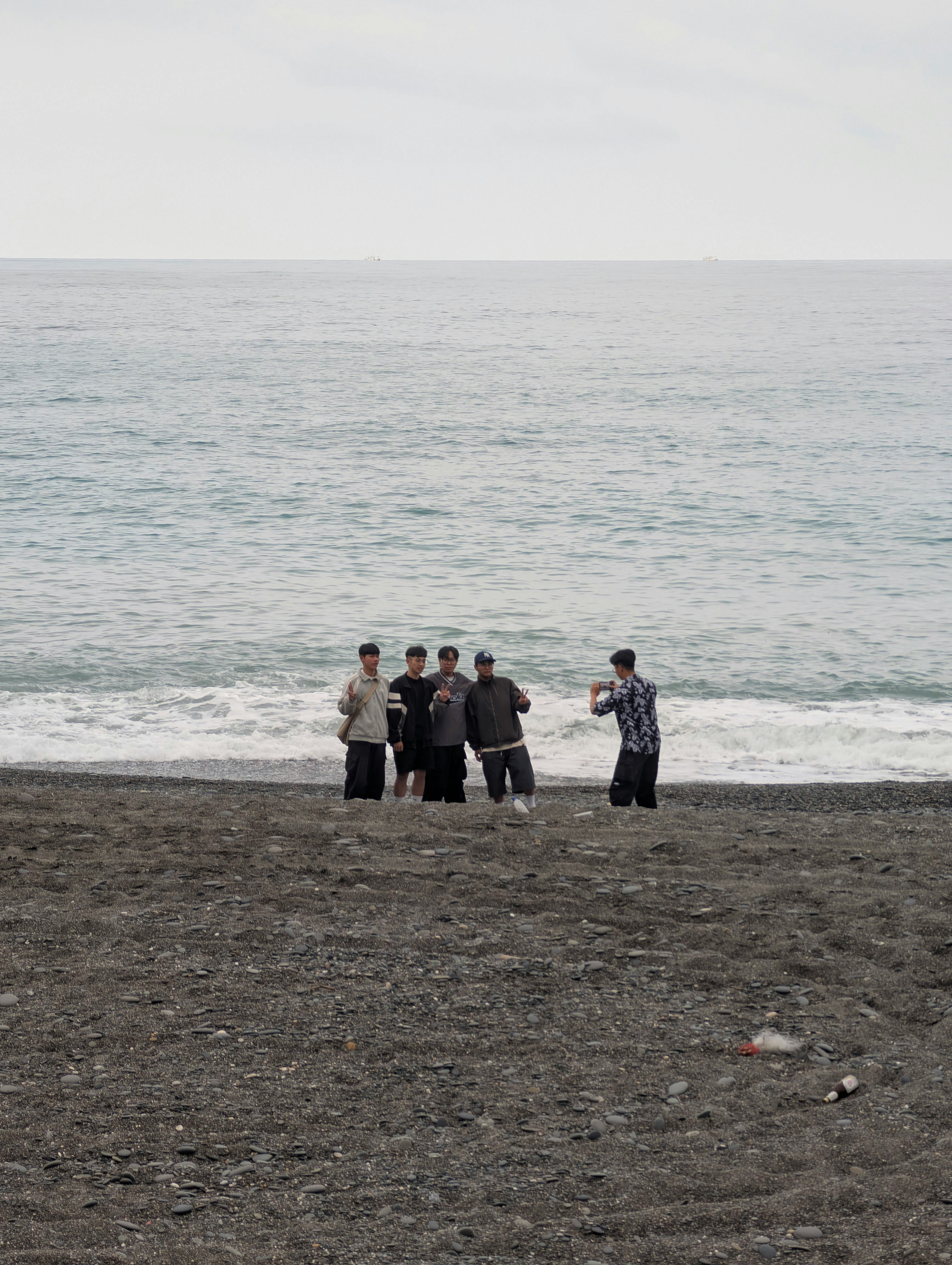 海辺の砂浜で並ぶ4人の友人とスマホ撮影
