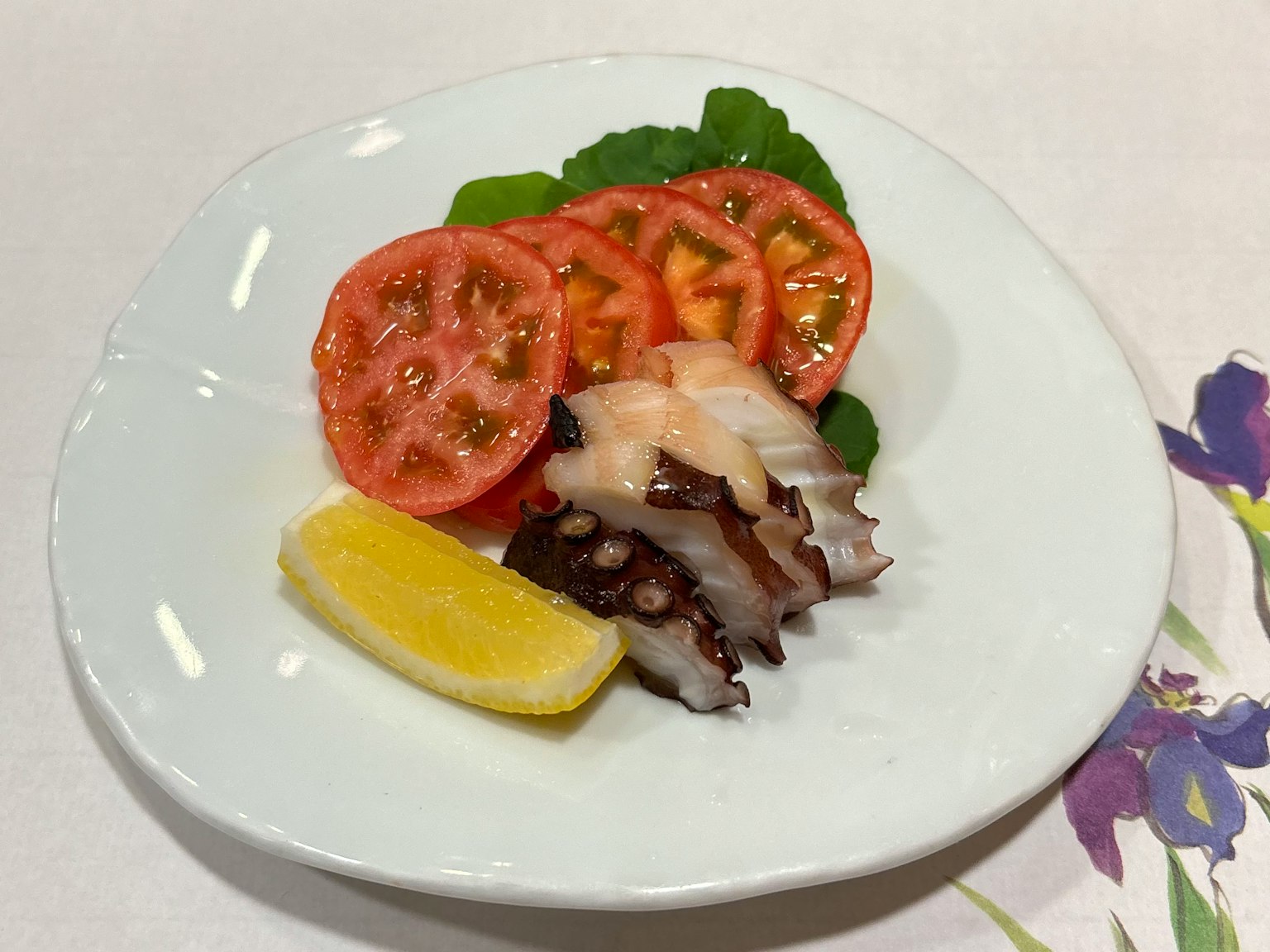 Octopus-Scheiben auf einem weißen Teller mit Tomatenscheiben und einem Zitronenschnitz