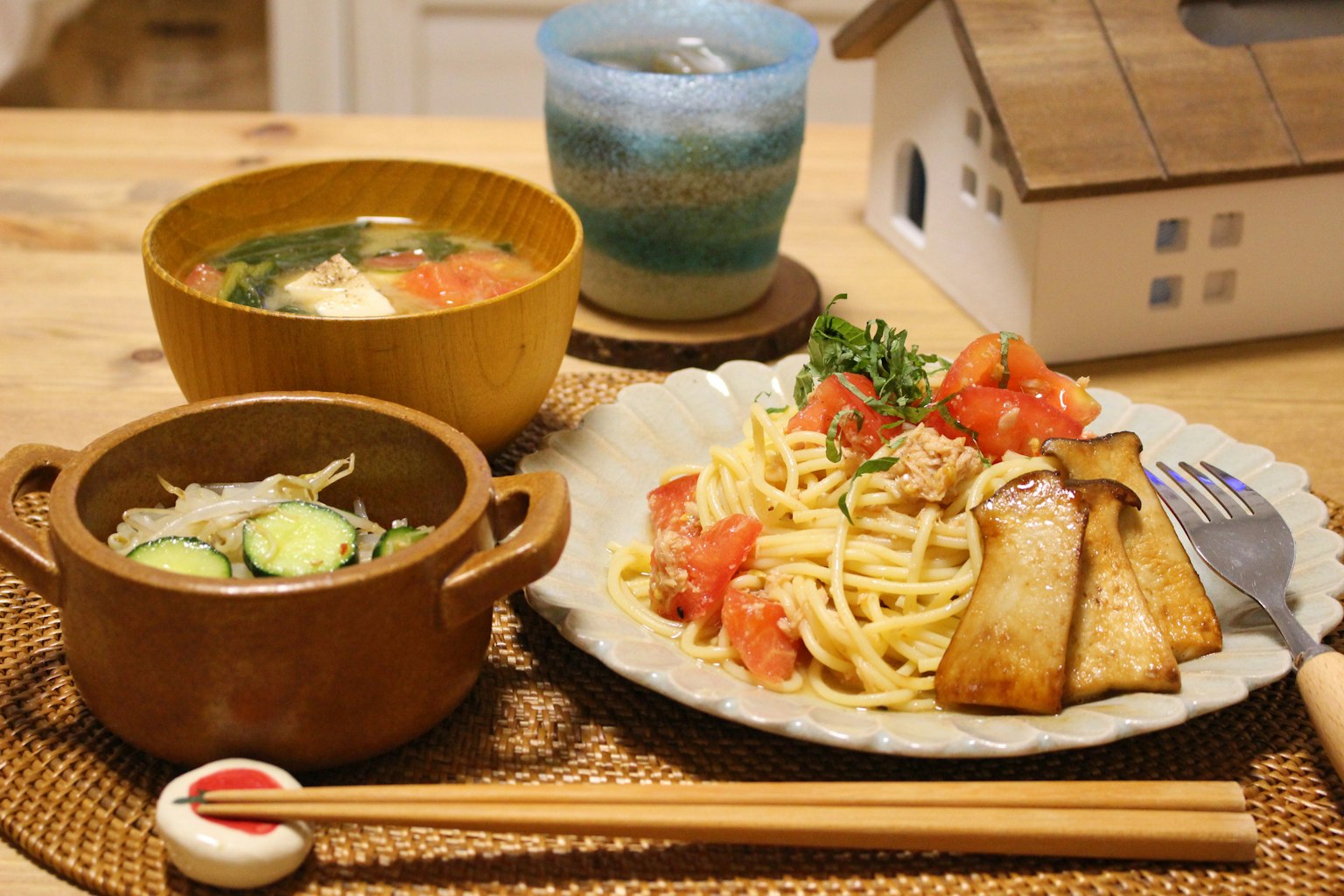 Assiette de spaghetti avec tomates et poisson grillé salade avec un bol de soupe et un verre bleu à proximité