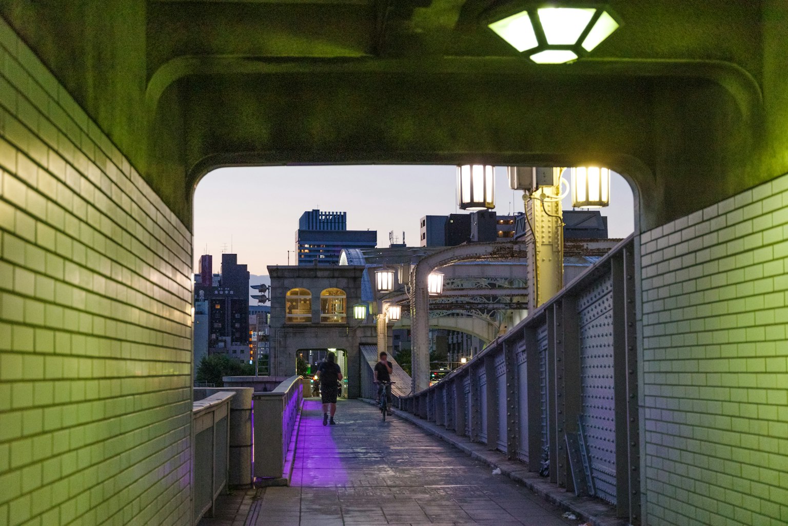 อุโมงค์สะพานที่มีแสงสีเขียวและทิวทัศน์เมืองยามเย็น