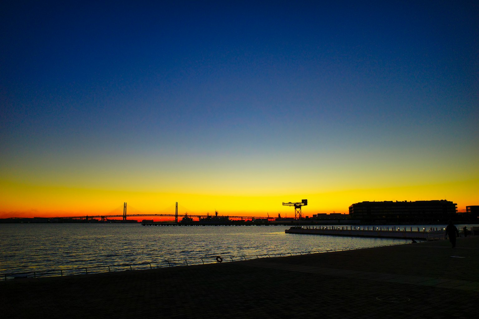 Silhouette of buildings against a vibrant sunset over the sea