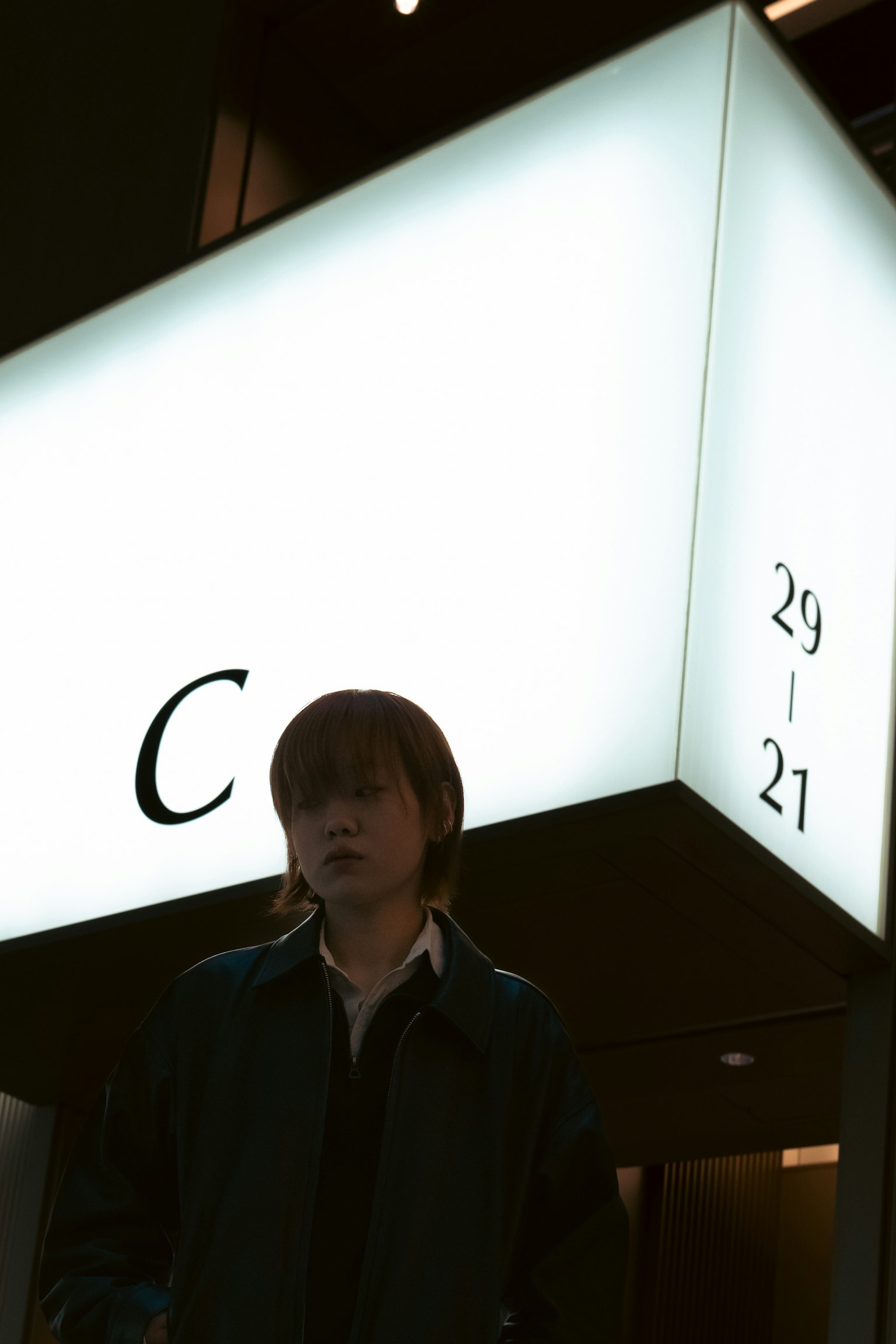 บุคคลยืนอยู่หน้าป้ายสีขาวที่มีตัวอักษร C และตัวเลข 29 21