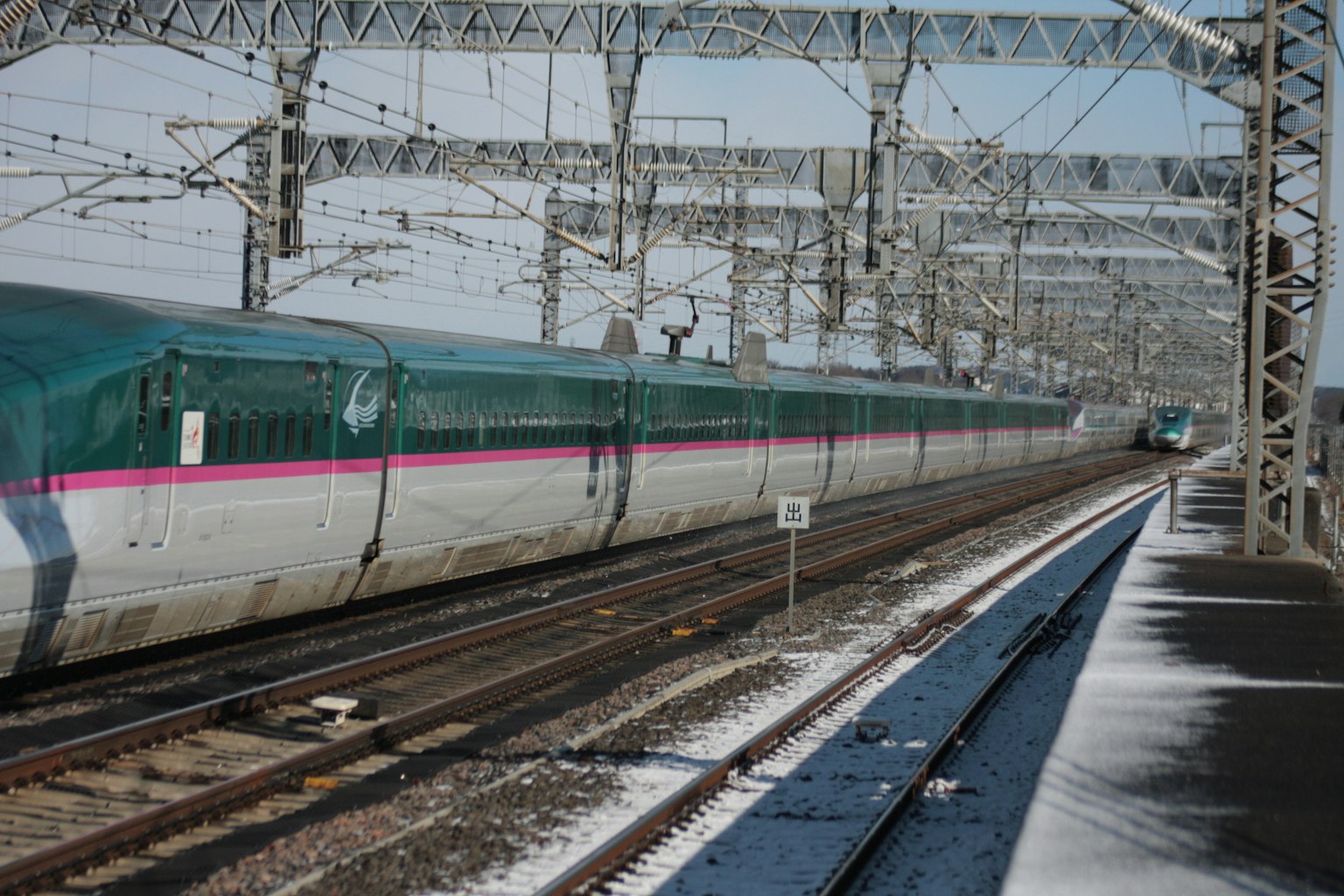 รถไฟชินคันเซนที่วิ่งผ่านภูมิทัศน์ที่มีหิมะพร้อมรางรถไฟ