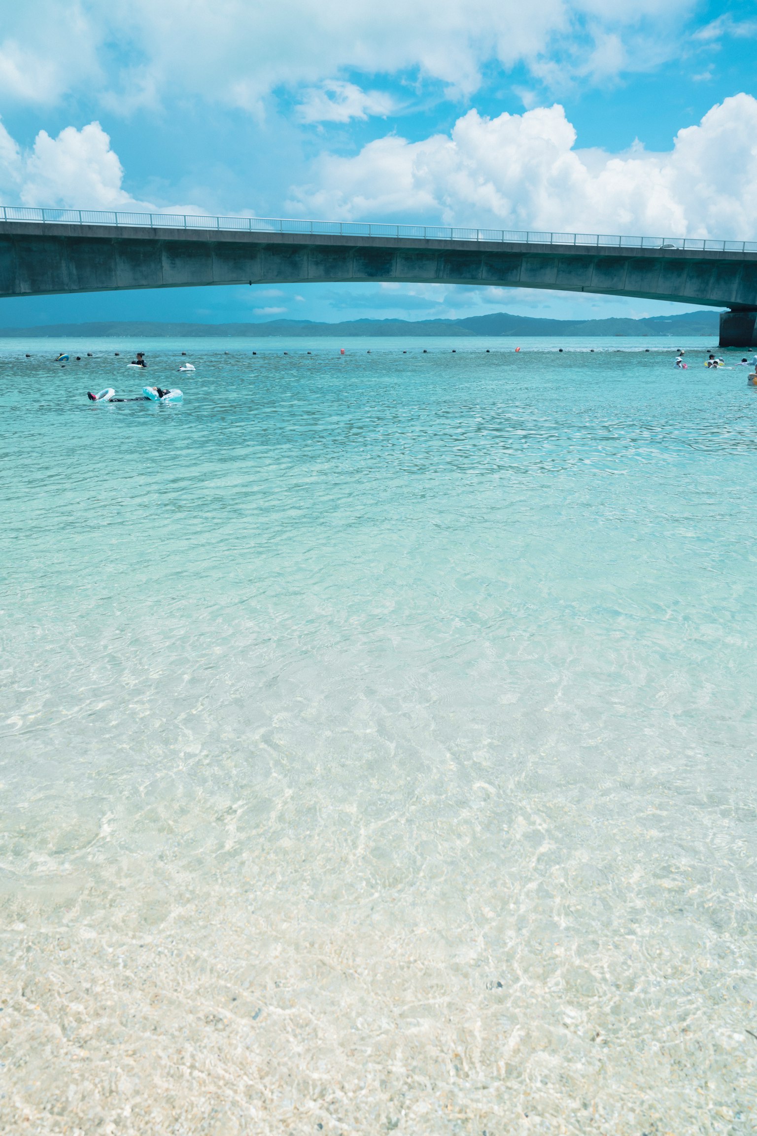 Hermosa vista del océano con agua clara y playa de arena debajo de un puente