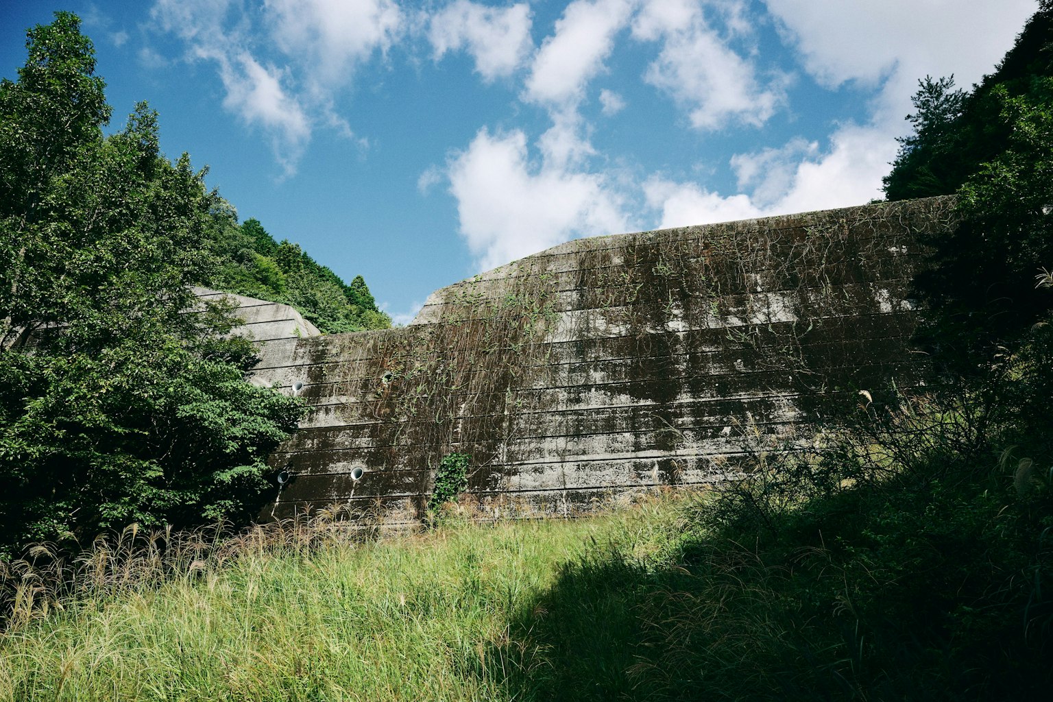 Old concrete wall surrounded by green grass and blue sky