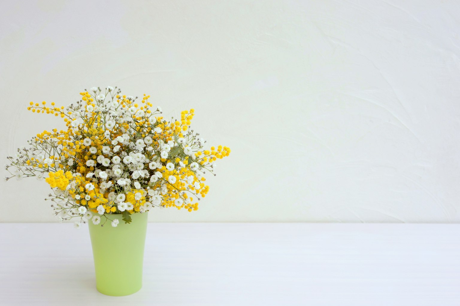 Un jarrón verde lleno de flores amarillas y blancas