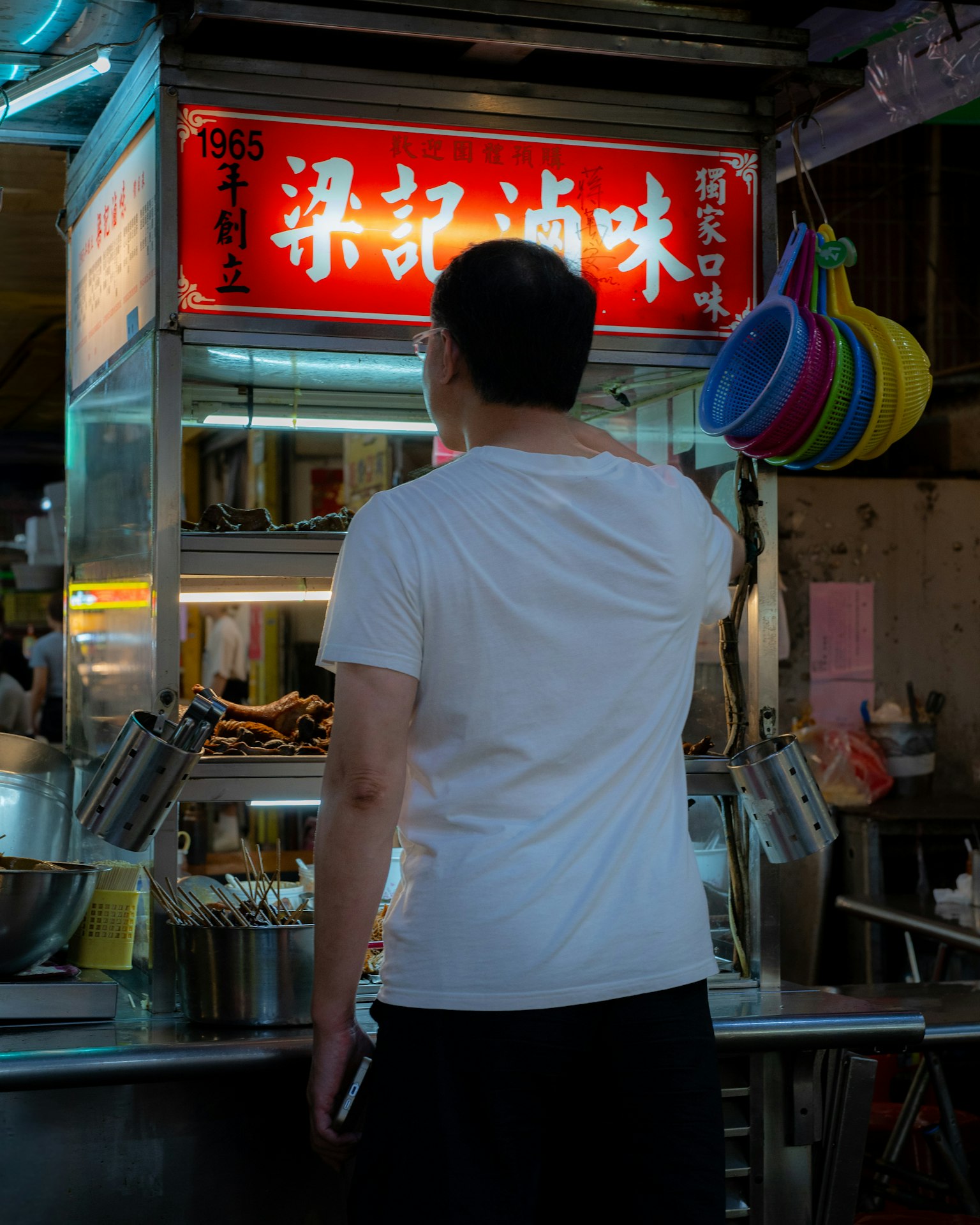 屋台で料理を選ぶ男性 白いTシャツと黒いパンツを着用 赤い看板に店名が書かれている