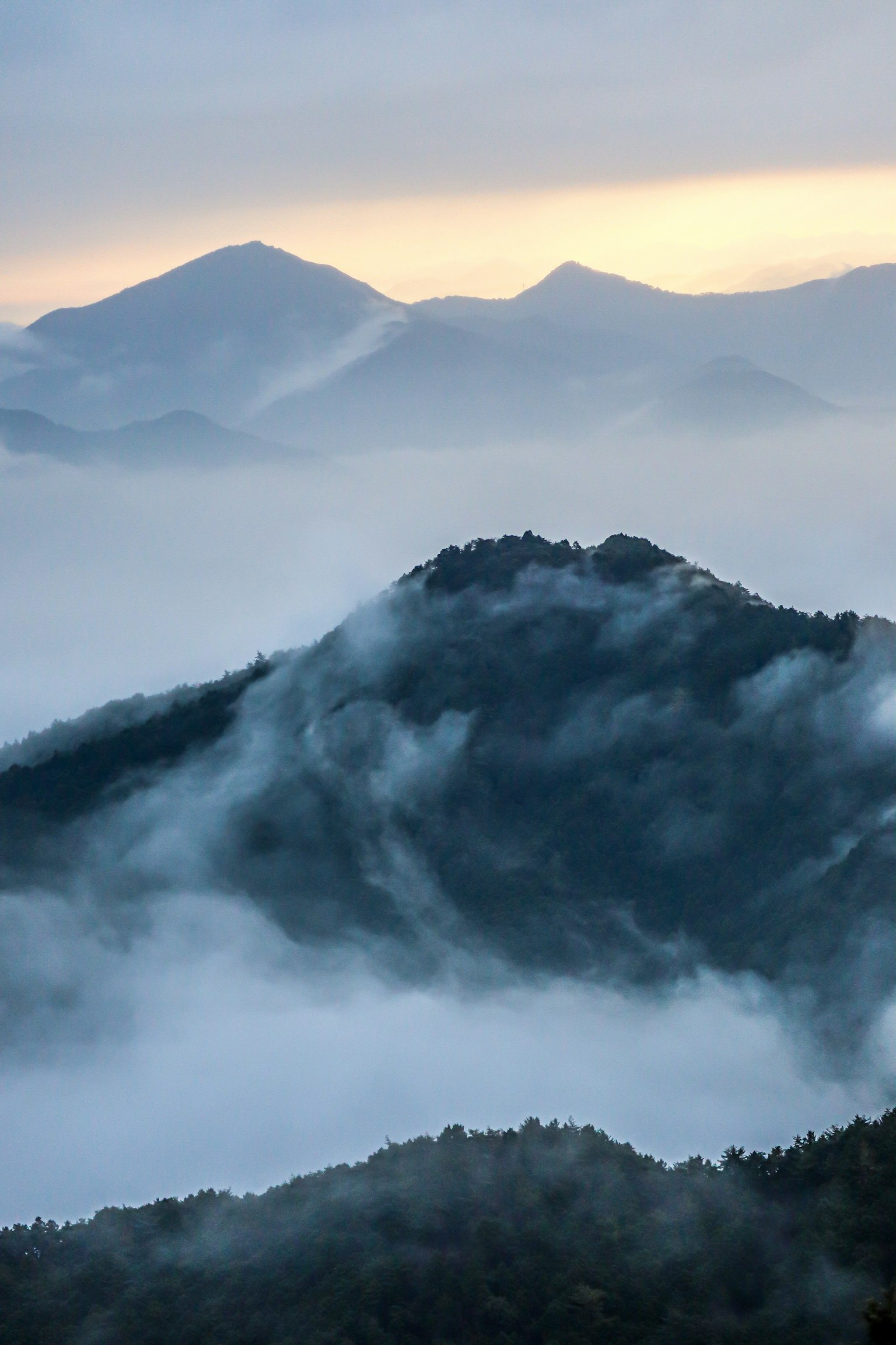 Montagne avvolte nella nebbia con un cielo blu morbido