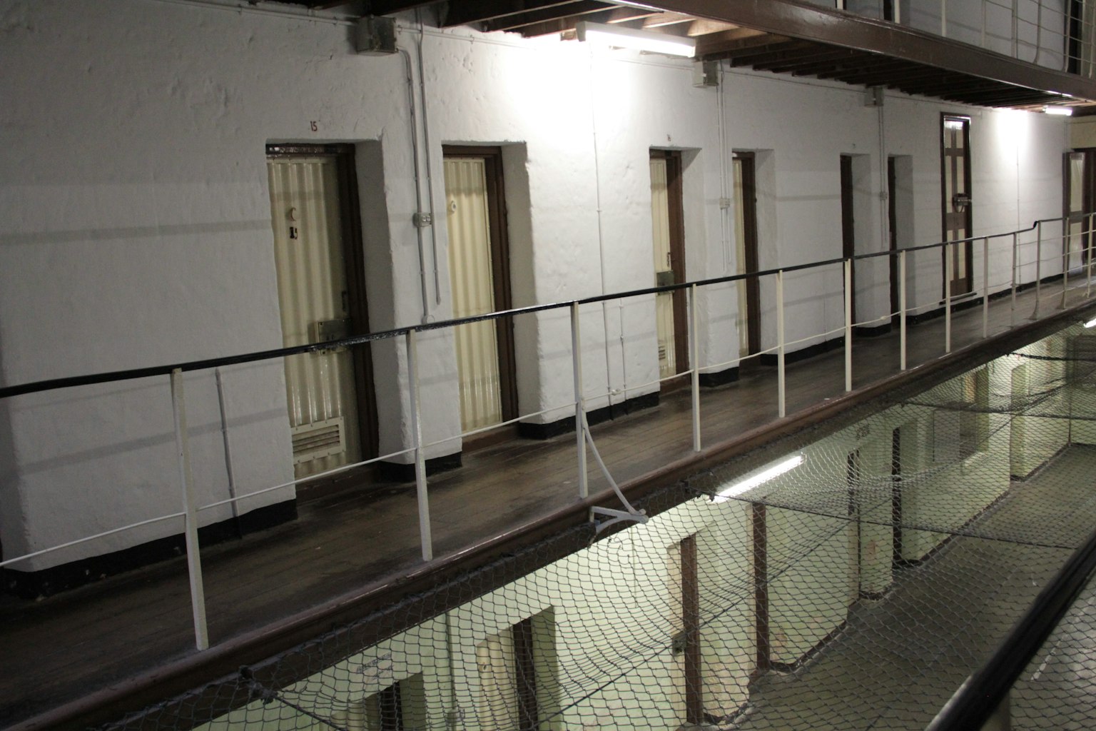 Prison corridor featuring lined cell doors and reflections