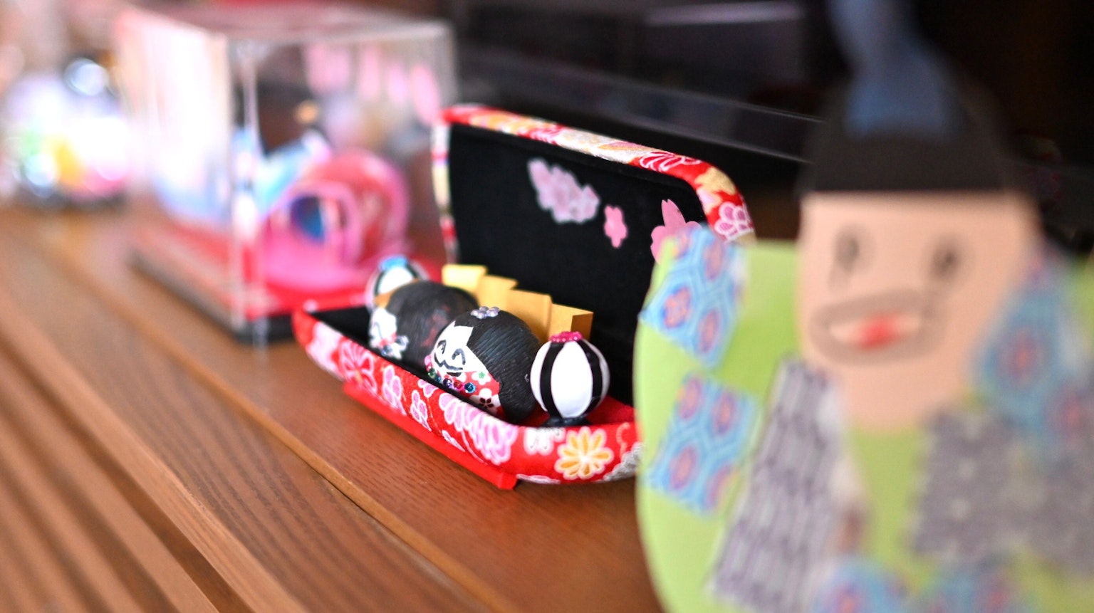 Model sushi kecil dalam kotak dekoratif merah dengan ornamen berwarna-warni di latar belakang