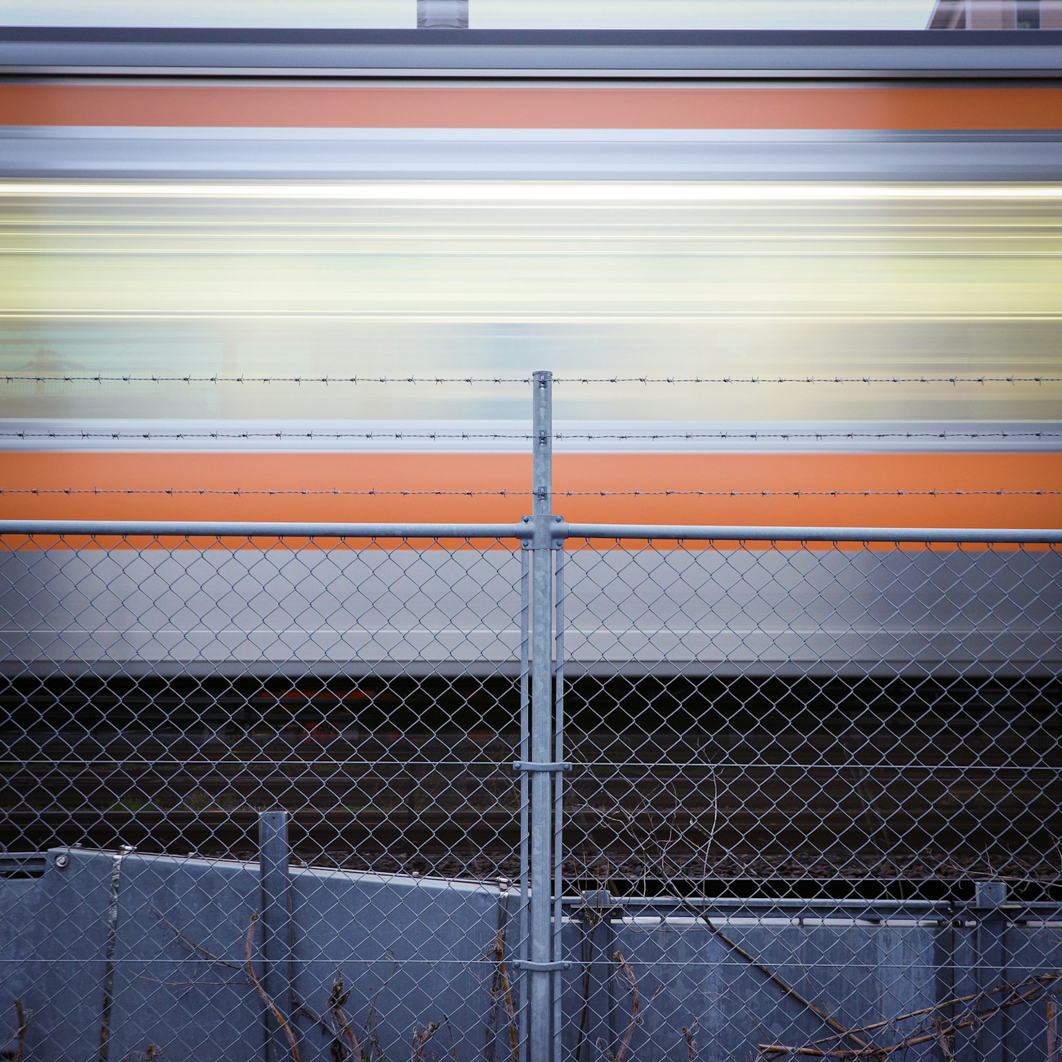 Desenfoque de movimiento de un tren pasando junto a una cerca de malla con rayas coloridas