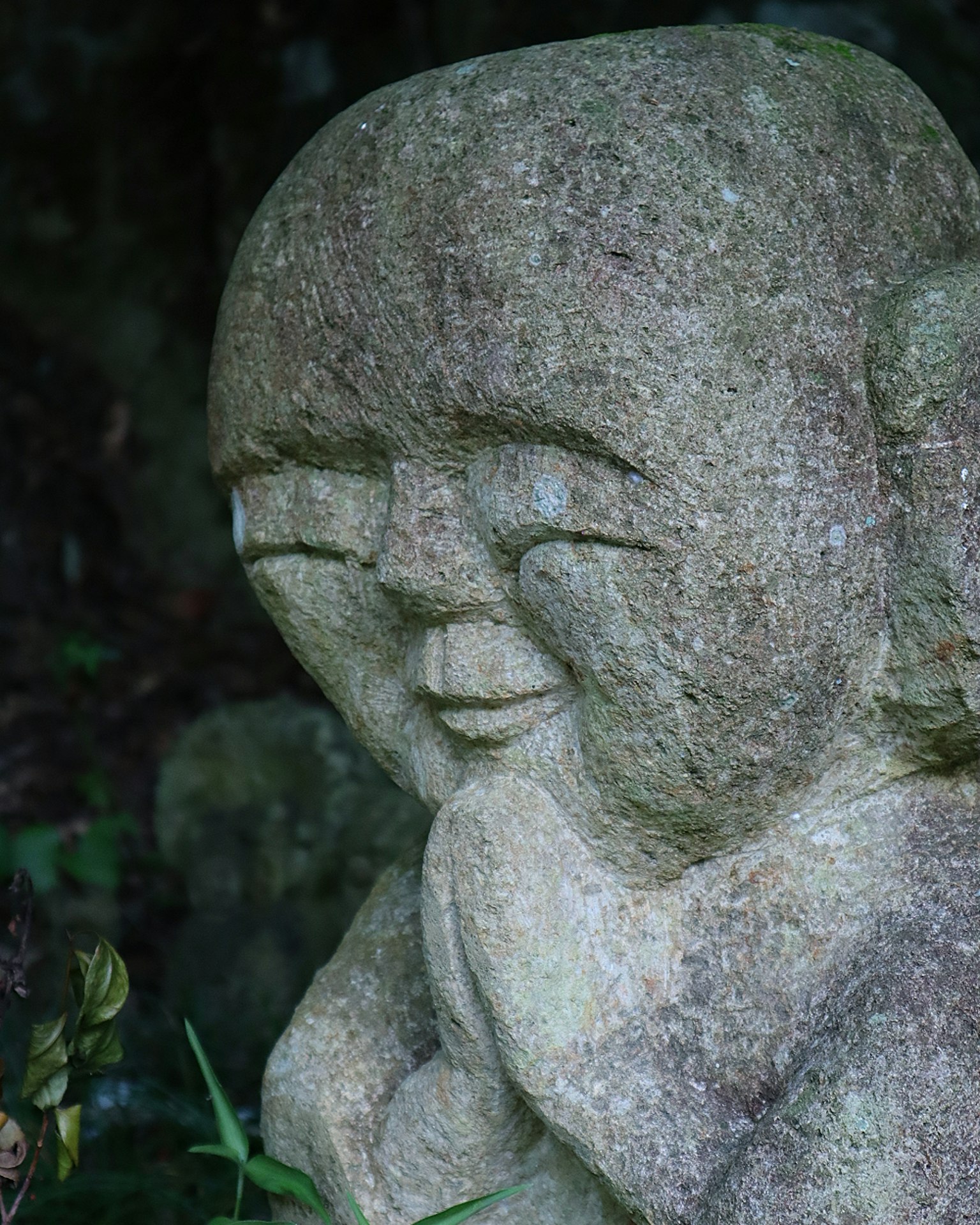 Una estatua de piedra de un niño sonriente rodeada de plantas verdes