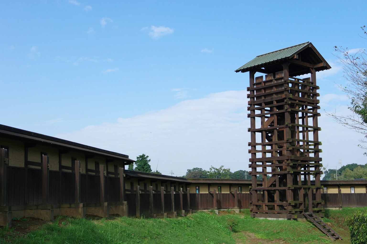 Torre de vigilancia de madera histórica con muros circundantes en un entorno natural