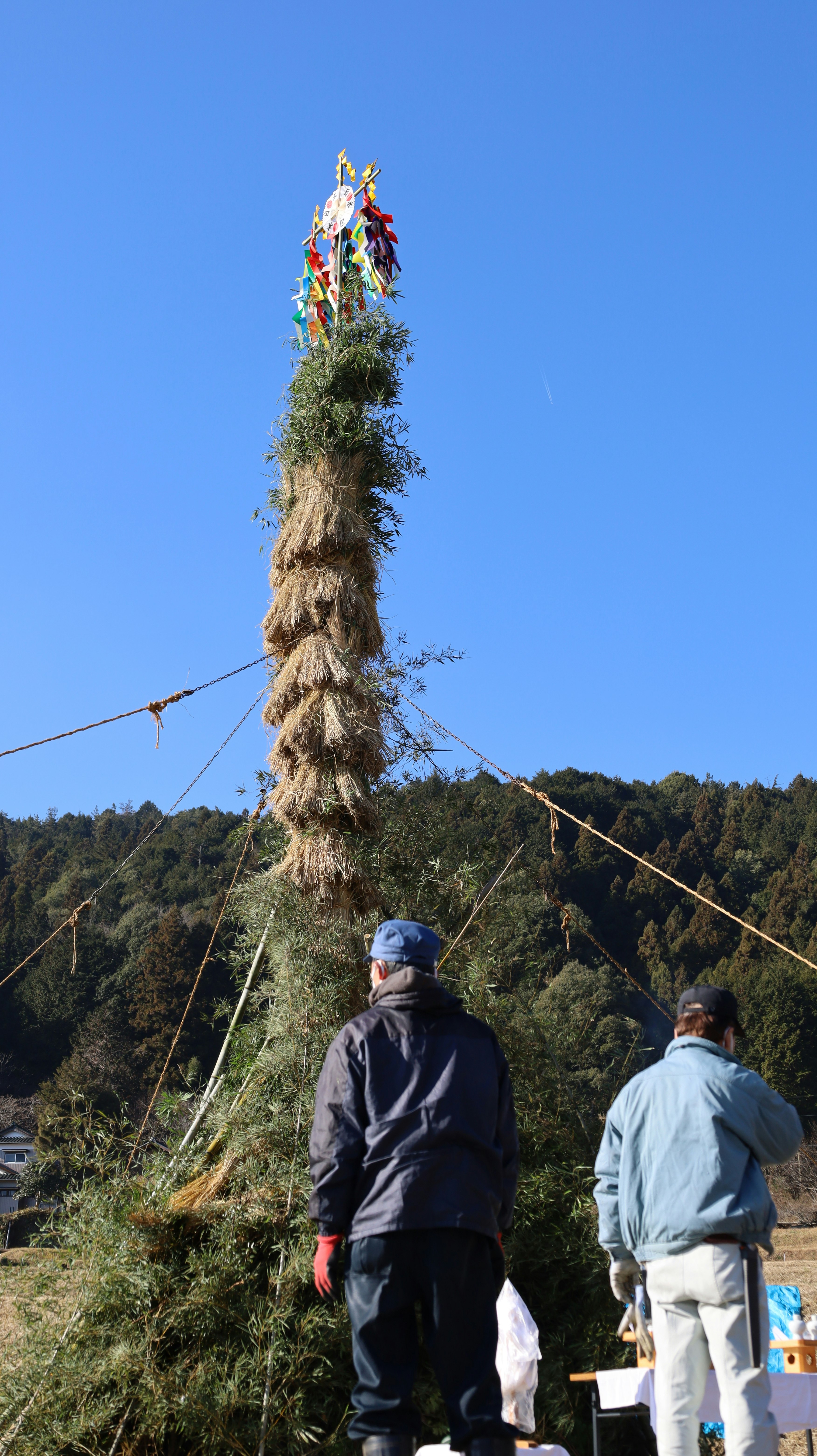 青空の下で山道を歩く人と注連縄のような飾り