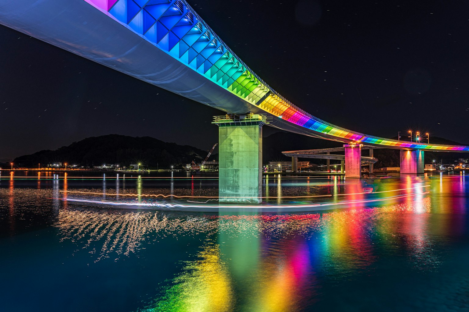 Jembatan berwarna cerah yang diterangi di malam hari dengan refleksi di air