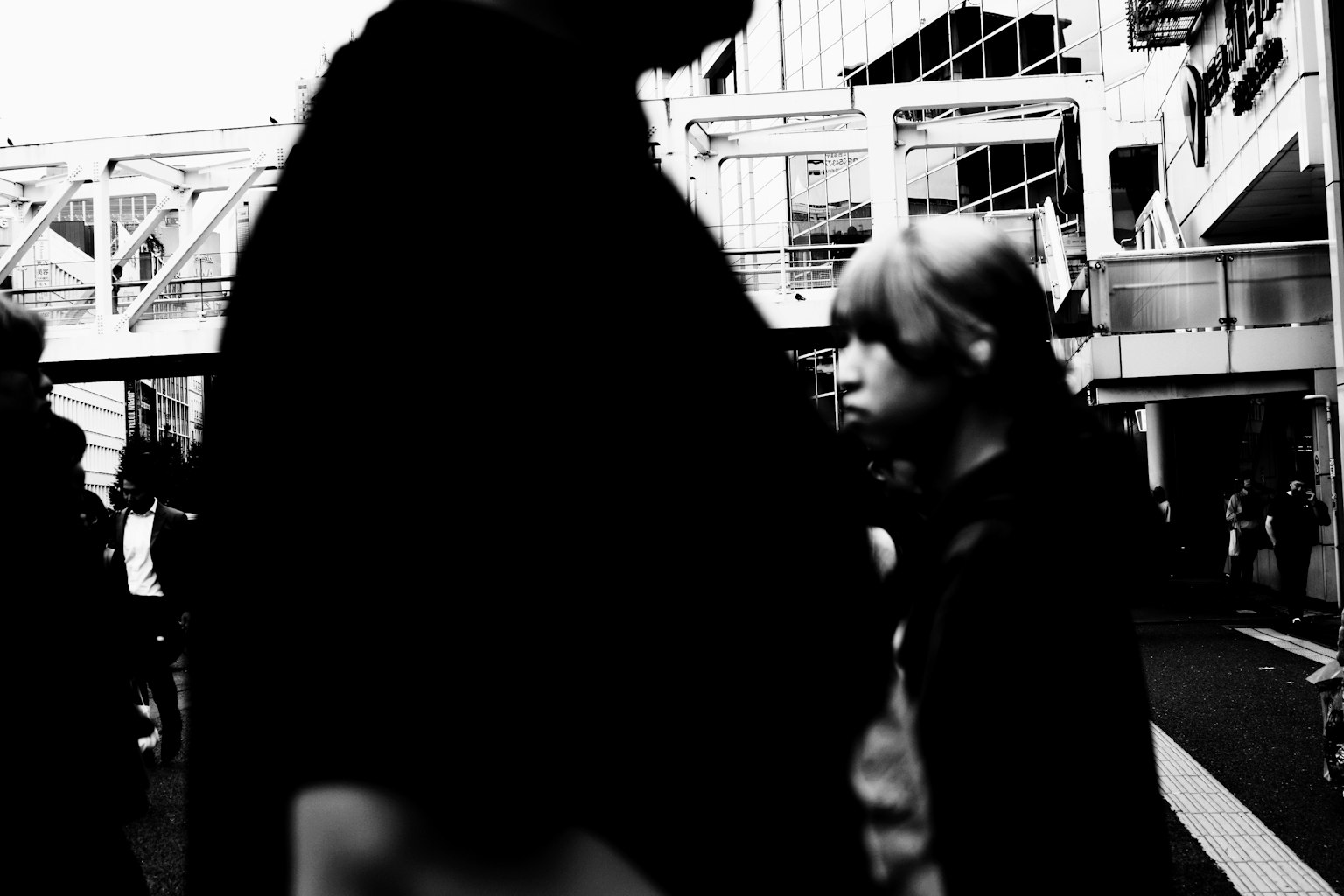 A boy standing quietly amidst a crowd with a shadowy adult nearby