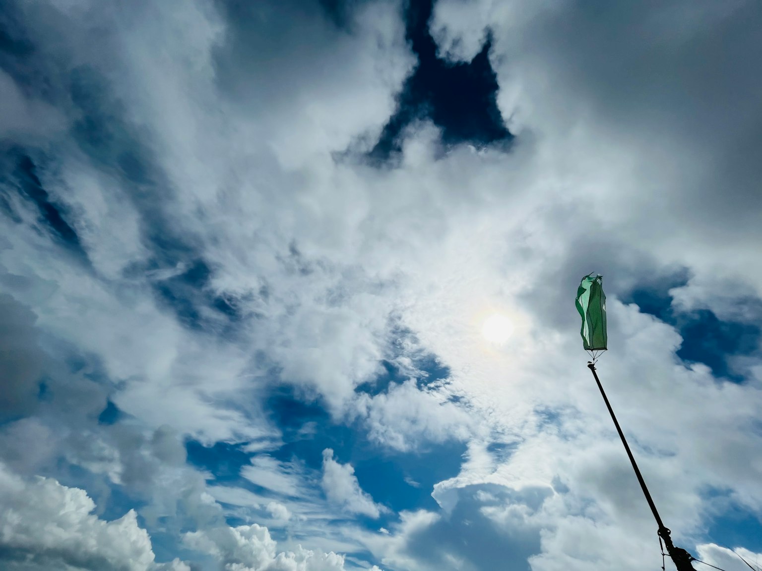 Hand hält eine grüne Fahne vor einem Hintergrund aus blauem Himmel und Wolken