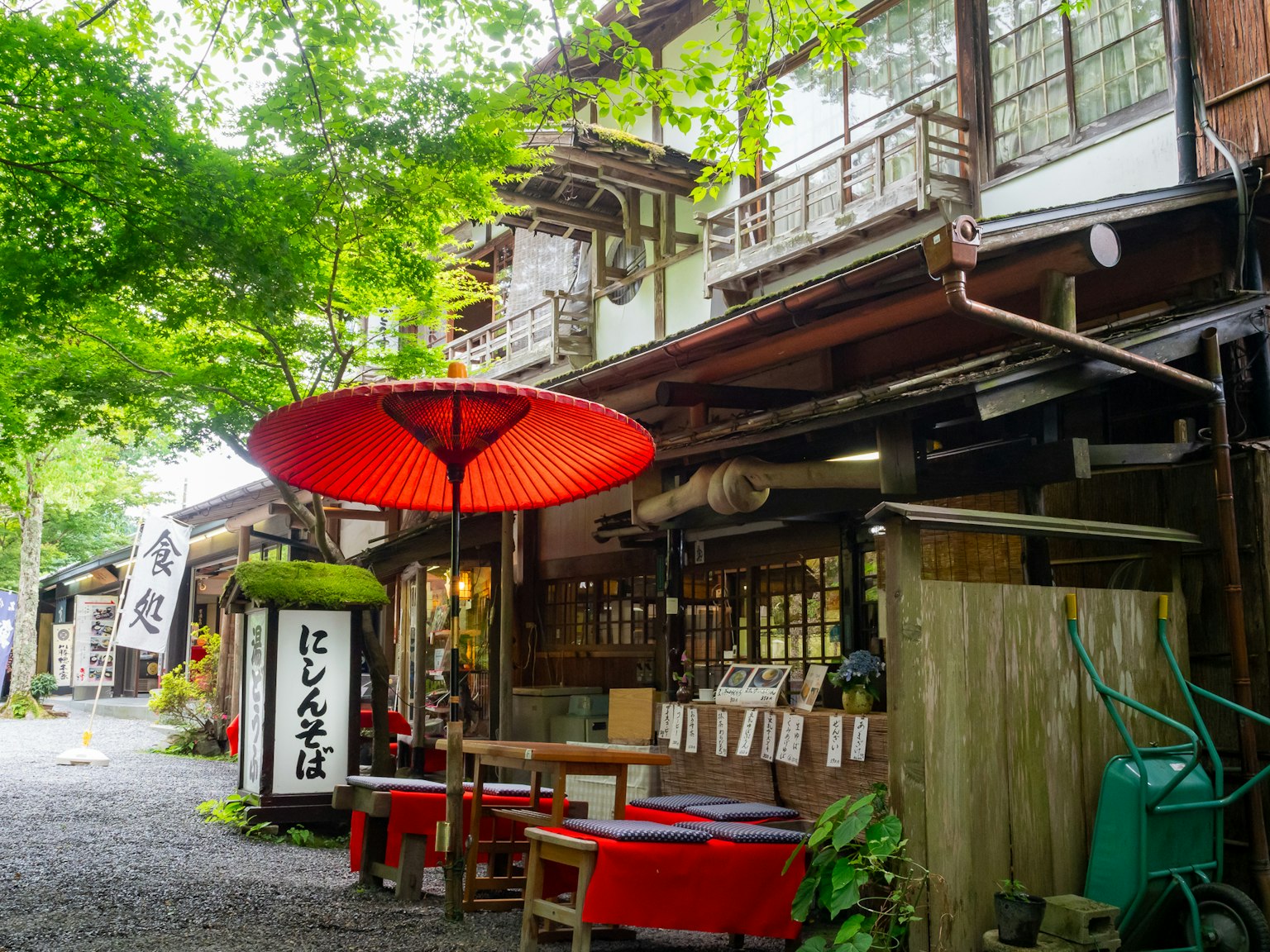 Escena de calle tradicional japonesa con una sombrilla roja sobre mesas y sillas rodeadas de vegetación exuberante