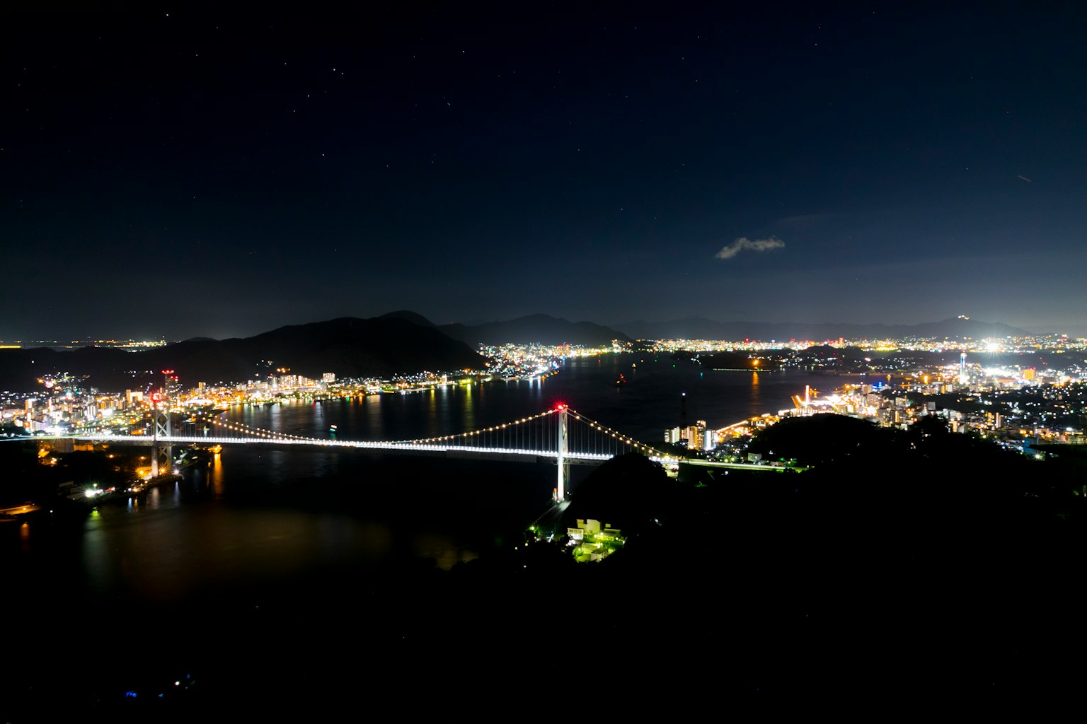 Vista escénica de un puente iluminado por la noche con luces de la ciudad