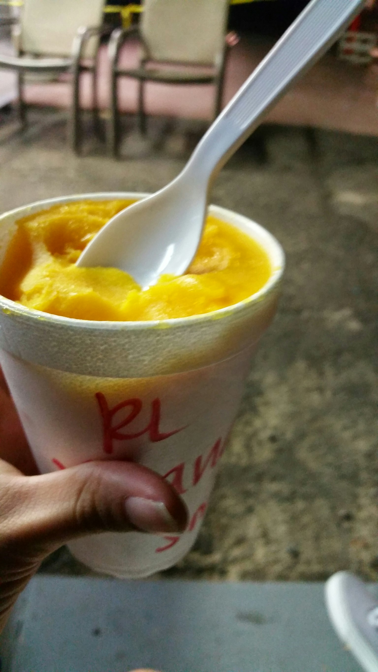 Un bicchiere di gelato al mango arancione tenuto in una mano con un cucchiaio bianco