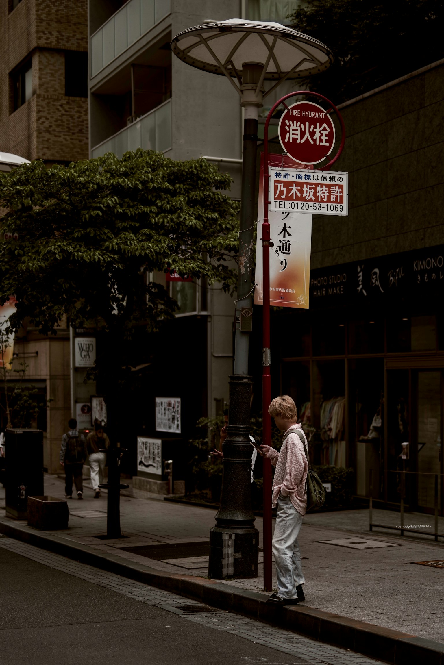 一名穿着白色衣服的男子在街角的公交站等候，周围有建筑物