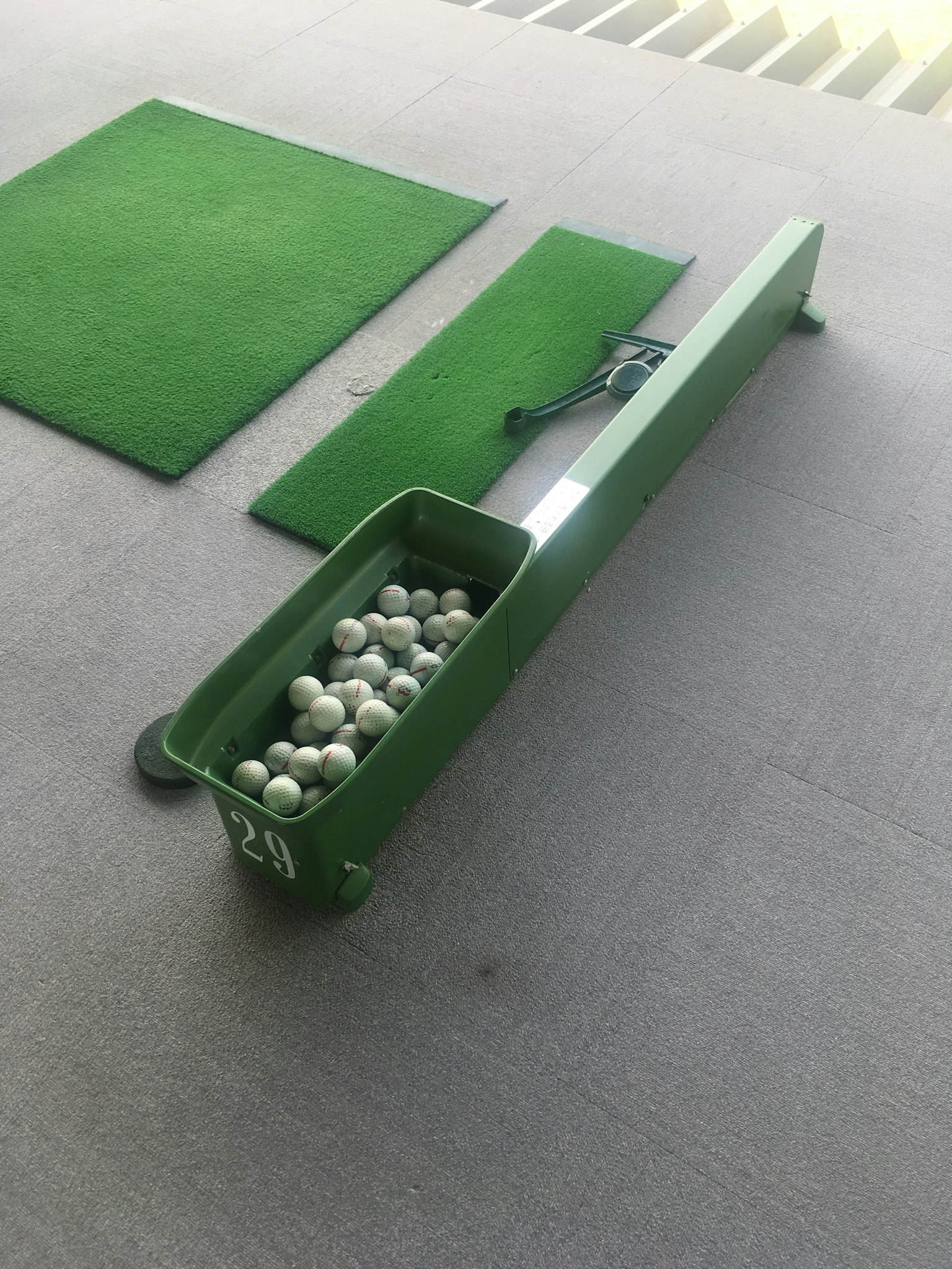 Una escena en un área de práctica de golf con una bandeja verde para bolas y alfombrillas