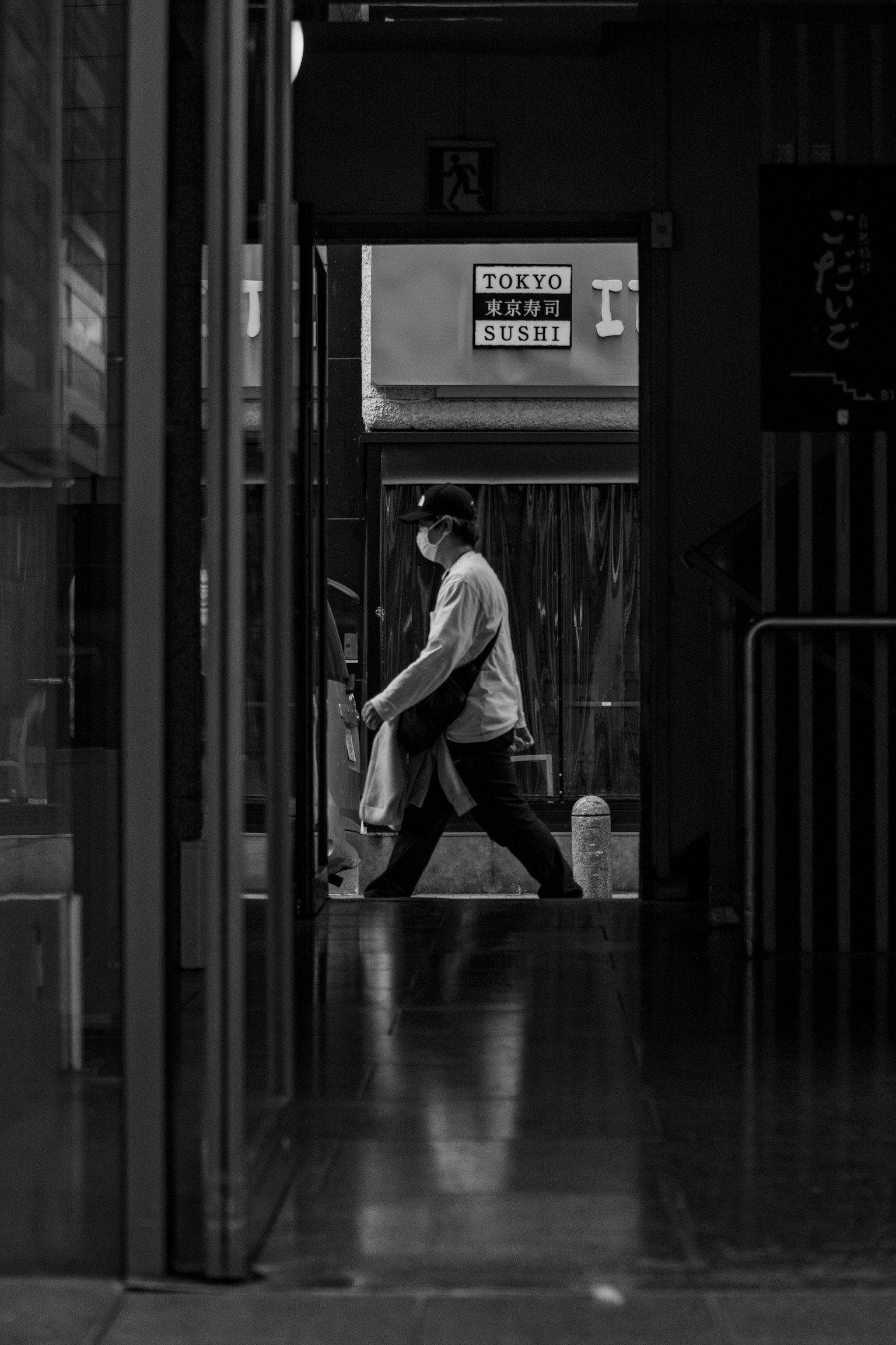 Foto en blanco y negro de una persona caminando por un pasillo suelo reflectante letreros de tiendas cercanas