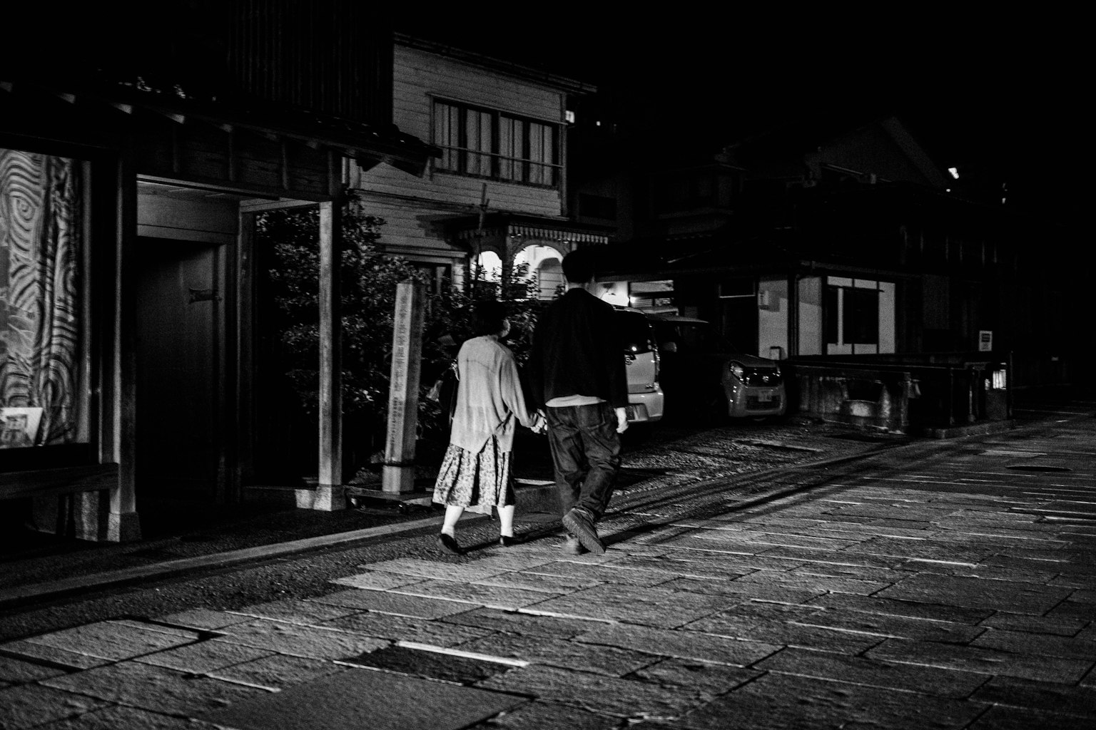 Siluet pria dan wanita berjalan bergandeng tangan di jalan malam