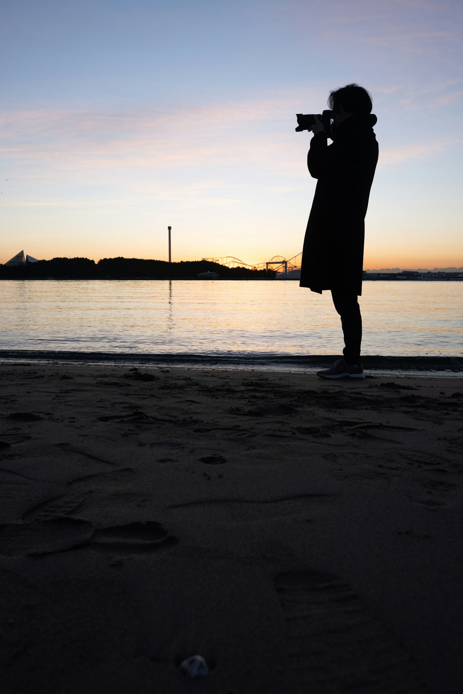 Silhouette di una persona che tiene una macchina fotografica sulla spiaggia al tramonto